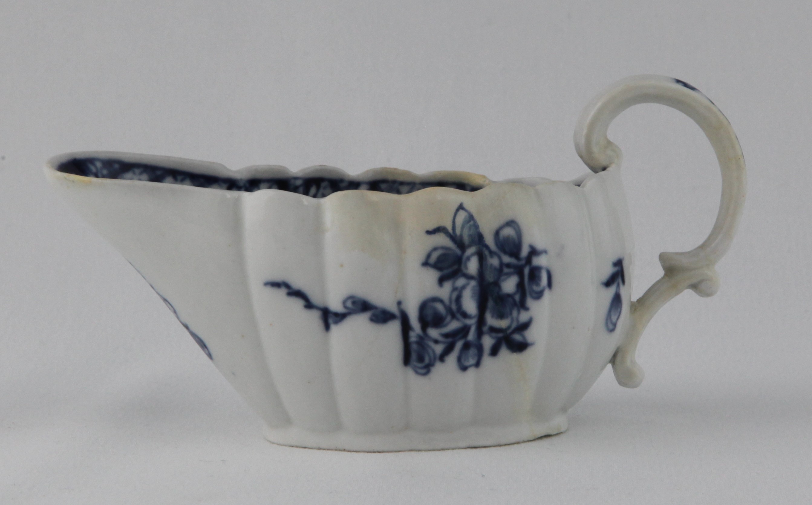 A Bristol fluted oval small sauceboat, with 'C' scroll handle, painted in underglaze blue with trailing flowers and leaves, the interior with a diaper band, and a flower head at the lip, 5 1/4" long, circa 1775, blue painted X mark