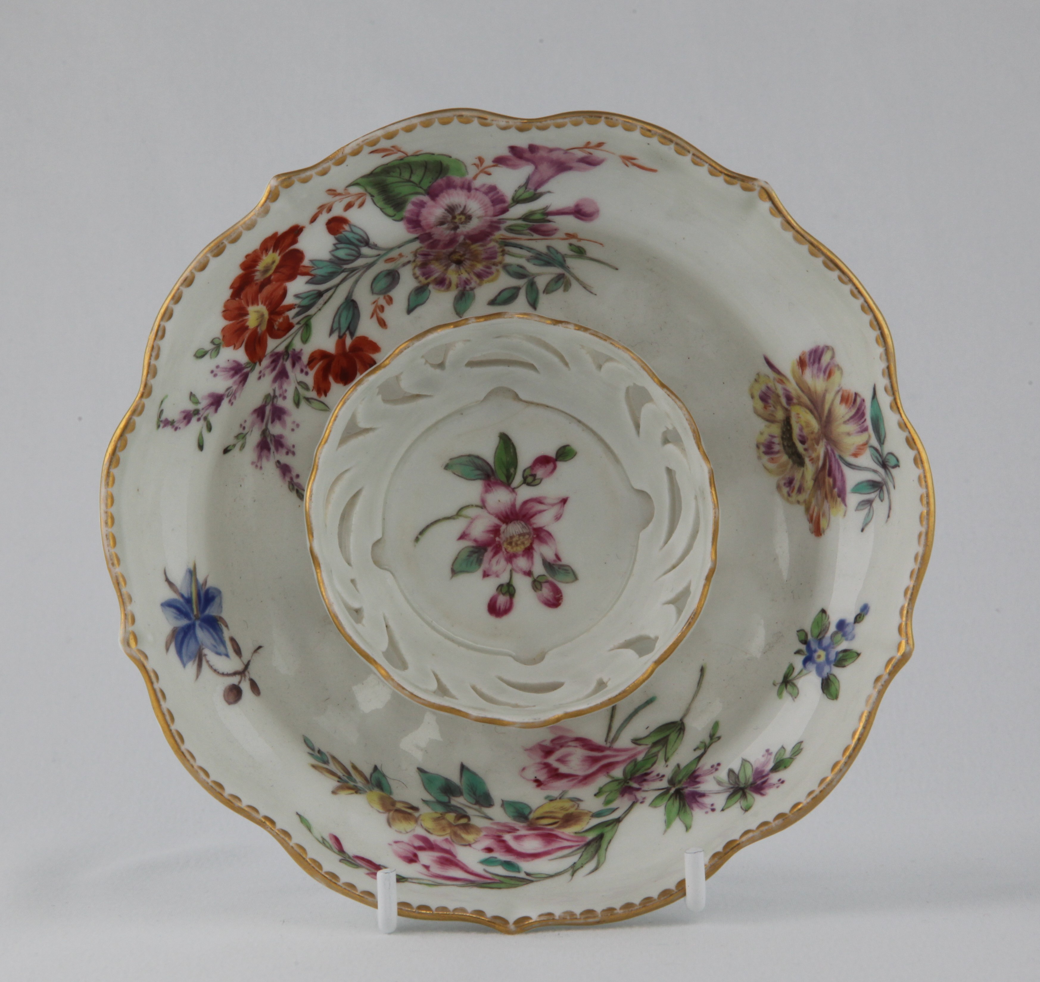 A rare Bristol ogee shaped trembleuse saucer,  particularly finely painted in coloured enamels with sprays of flowers and leaves, and scattered flowers, within gilt dentil borders, 5 1/2" diameter overall, circa 1775, B7 mark in blue enamel