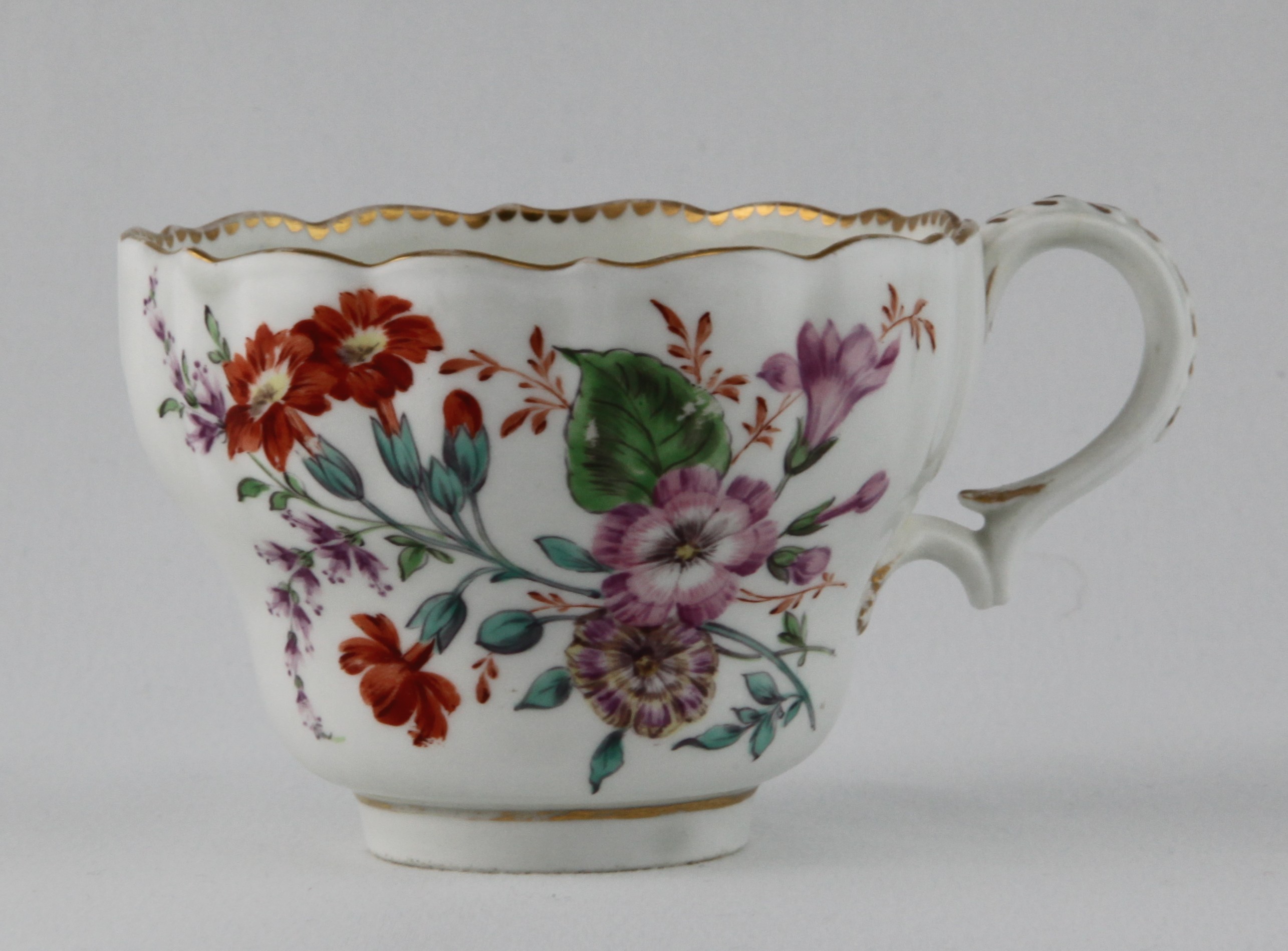 A rare Bristol ogee shaped chocolate cup with laurel moulded loop handle, particularly finely painted in coloured enamels with sprays of flowers and leaves, and scattered flowers, within gilt dentil borders, 5 1/2" diameter overall, circa 1775, B7 mark in blue enamel