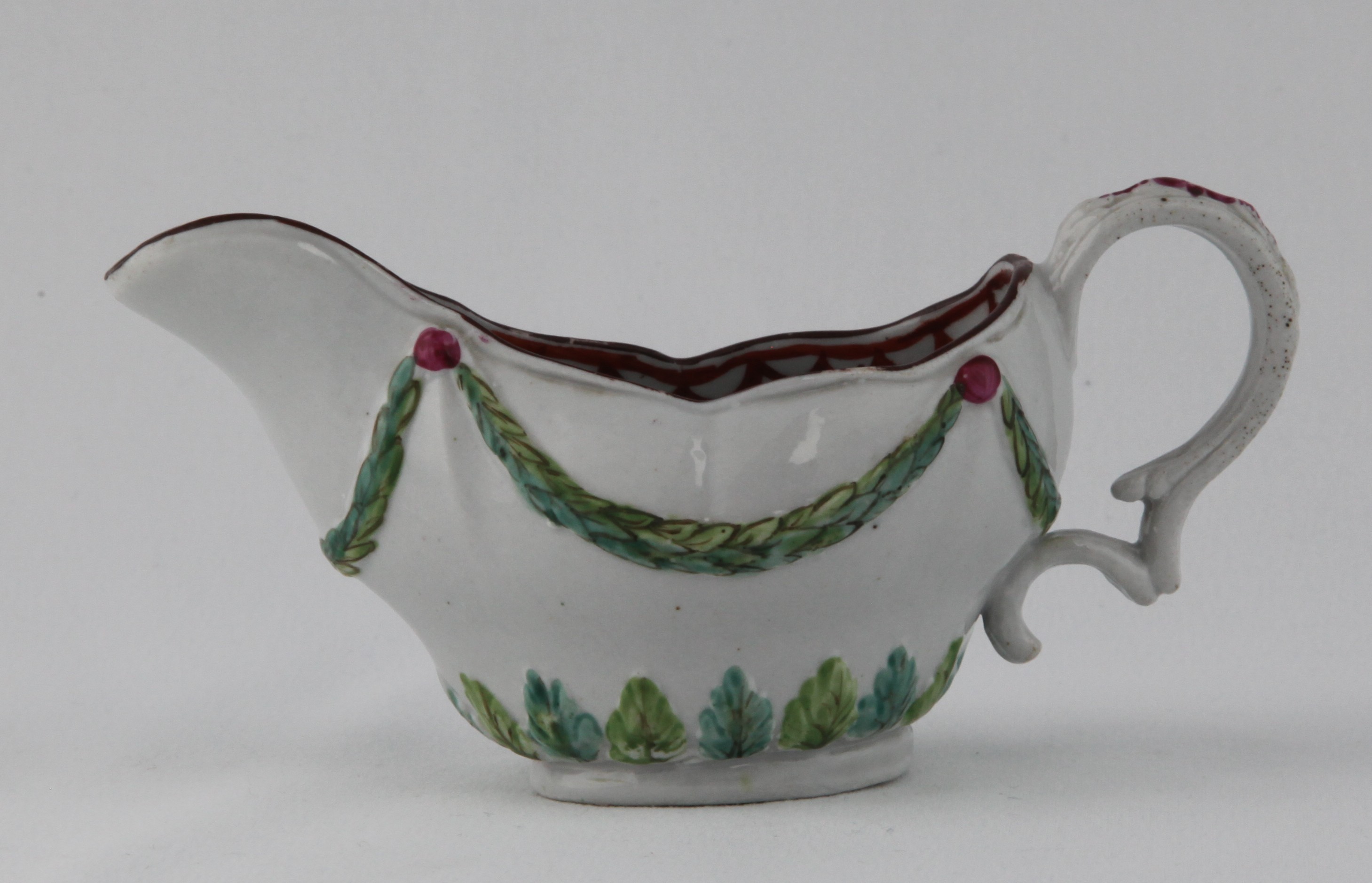 An unusual Bristol small ogee shaped oval sauce boat, with harebell moulded scroll handle, moulded in relief with laurel swags, picked out in green, and suspended from puce rosettes, above a stiff leaf moulded band, brown line rim, the interior painted in iron red with a stiff leaf and looped band, 5 1/2" long,  circa 1775, no mark