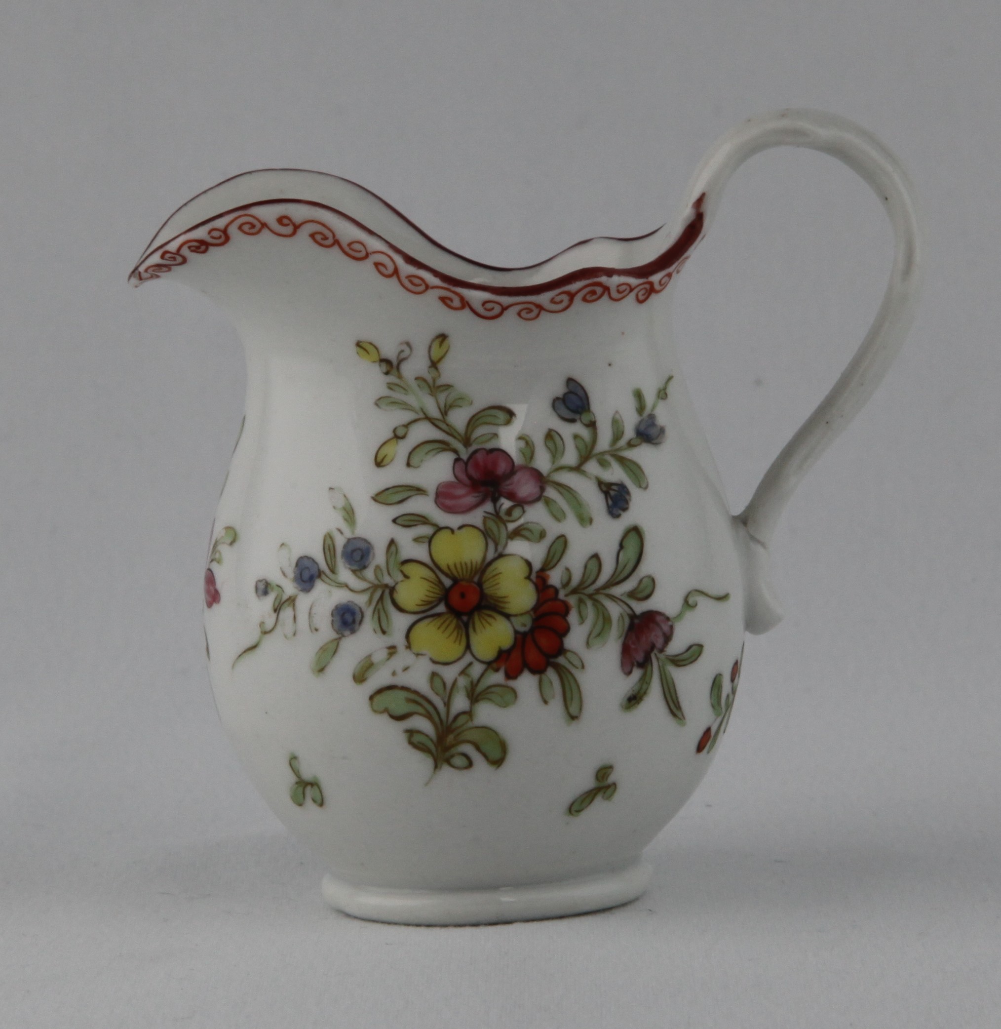 A rare Bristol small baluster shaped cream jug, with crabstock loop handle and shaped rim, painted in coloured enamels with a bold spray of flowers and leaves, and scattered flowers, beneath an iron red scroll band, brown line rim, 3" high, circa 1775, blue painted X mark