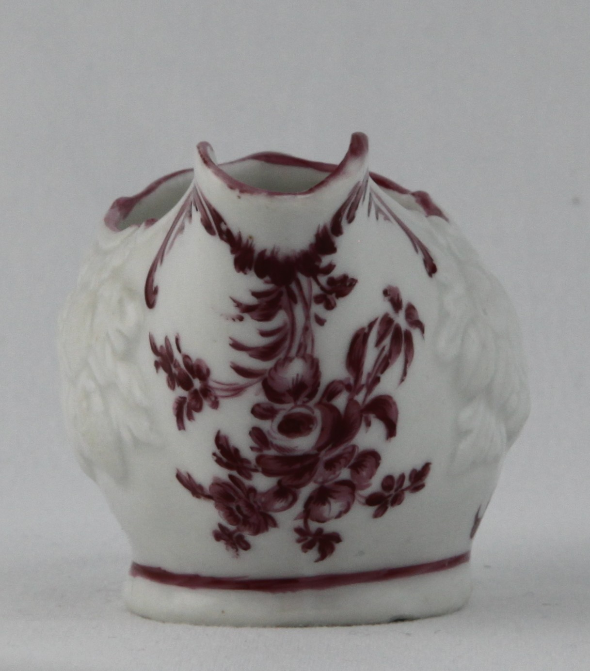 A Bristol small oval butter boat, with loop handle, crisply moulded in relief with two clusters of fruits and leaves, and painted in puce monochrome with flowers and leaves, within puce line borders, 4 1/4" long, circa 1770, no mark