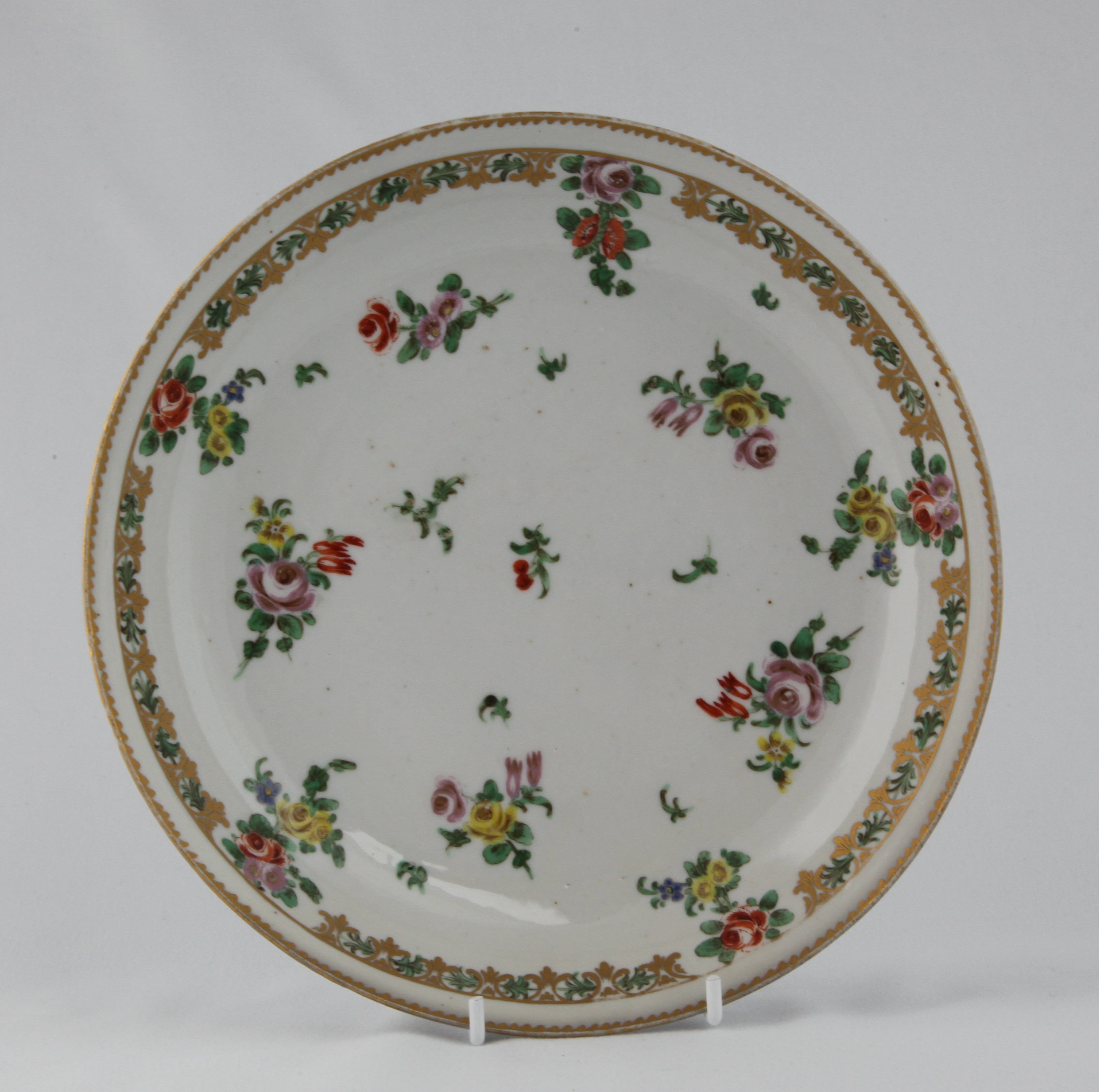 A Bristol saucer dish, painted in coloured enamels with scattered flowers and leaves, within a gilt border panelled with flowers and leaves, 8 1/4" diameter, circa 1772, no mark