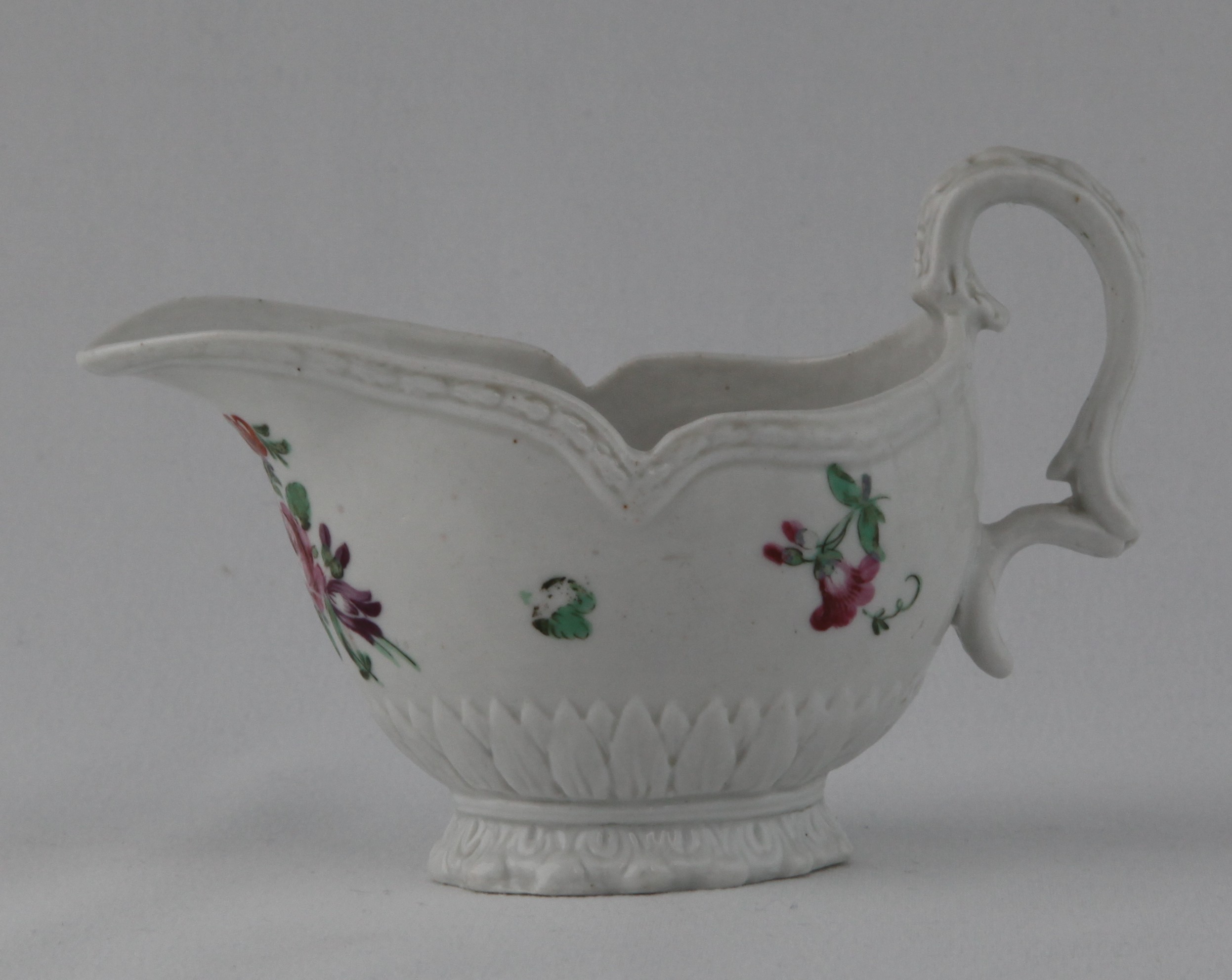 A Bristol oval sauce boat, with harebell moulded scroll handle, painted in coloured enamels with a flower spray and scattered flowers, beneath a boldly shaped moulded rim, the base with a stiff leaf moulded band, and leaf moulded spreading foot, 5" long, circa 1770, blue painted X mark and numeral 10