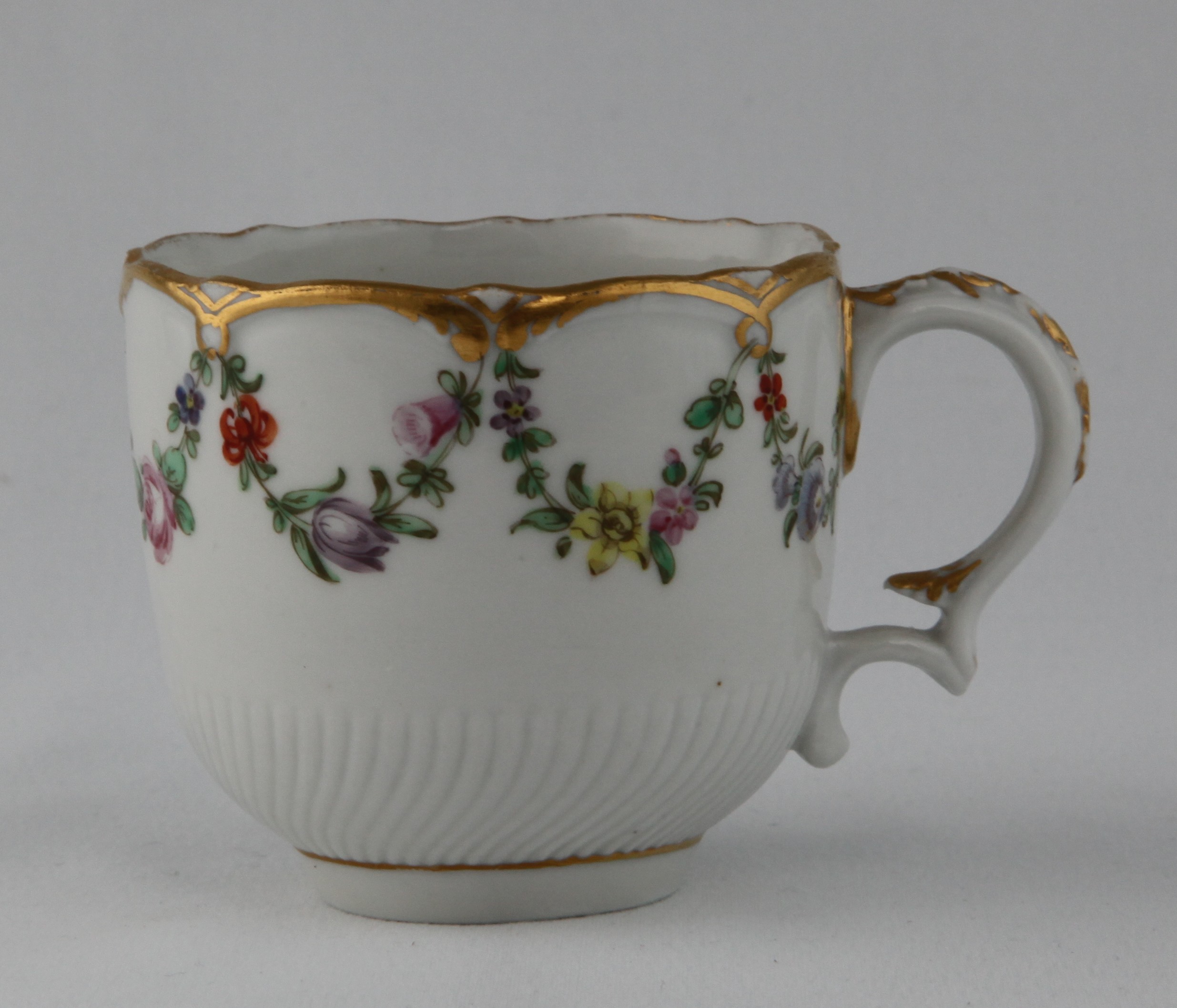 A Bristol coffee cup with harebell moulded ear shaped handle, painted in coloured enamels with swags of flowers and leaves, suspended from gilt loops, on a part spirally fluted ground, within gilt 'C' scroll borders, circa 1774-75, blue painted X marks and numeral 1