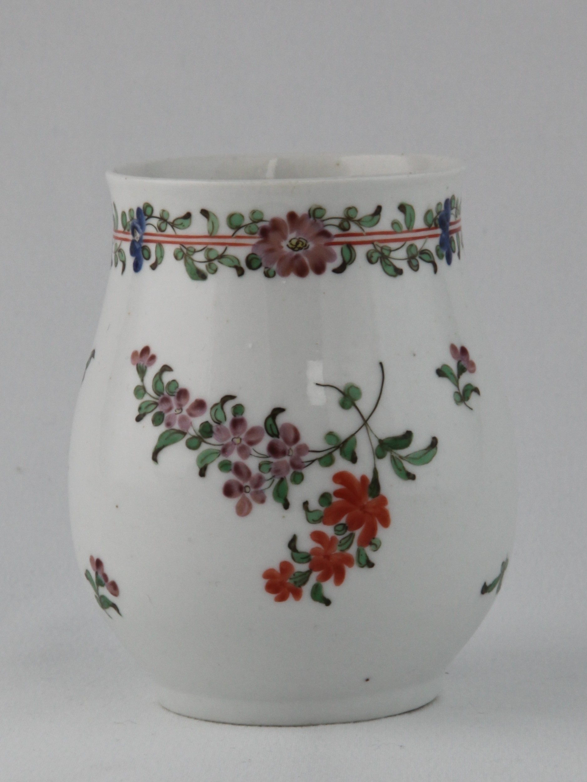 A Bristol baluster shaped small mug, with notched loop handle, painted in coloured enamels with scattered flowers, beneath two iron red bands entwined with flowers and leaves, 4" high, circa 1772-74, no mark