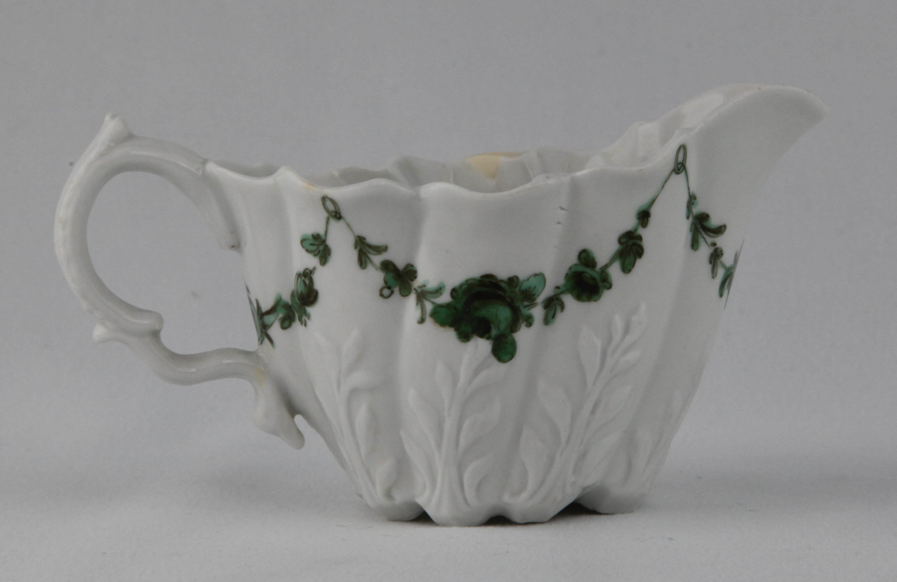 An unusual Bristol 'Low Chelsea Ewer' cream boat, painted in green monochrome with swags of flowers and leaves, suspended from green loops, 4 3/4" long, circa 1774-75, blue painted X mark and numeral 6
