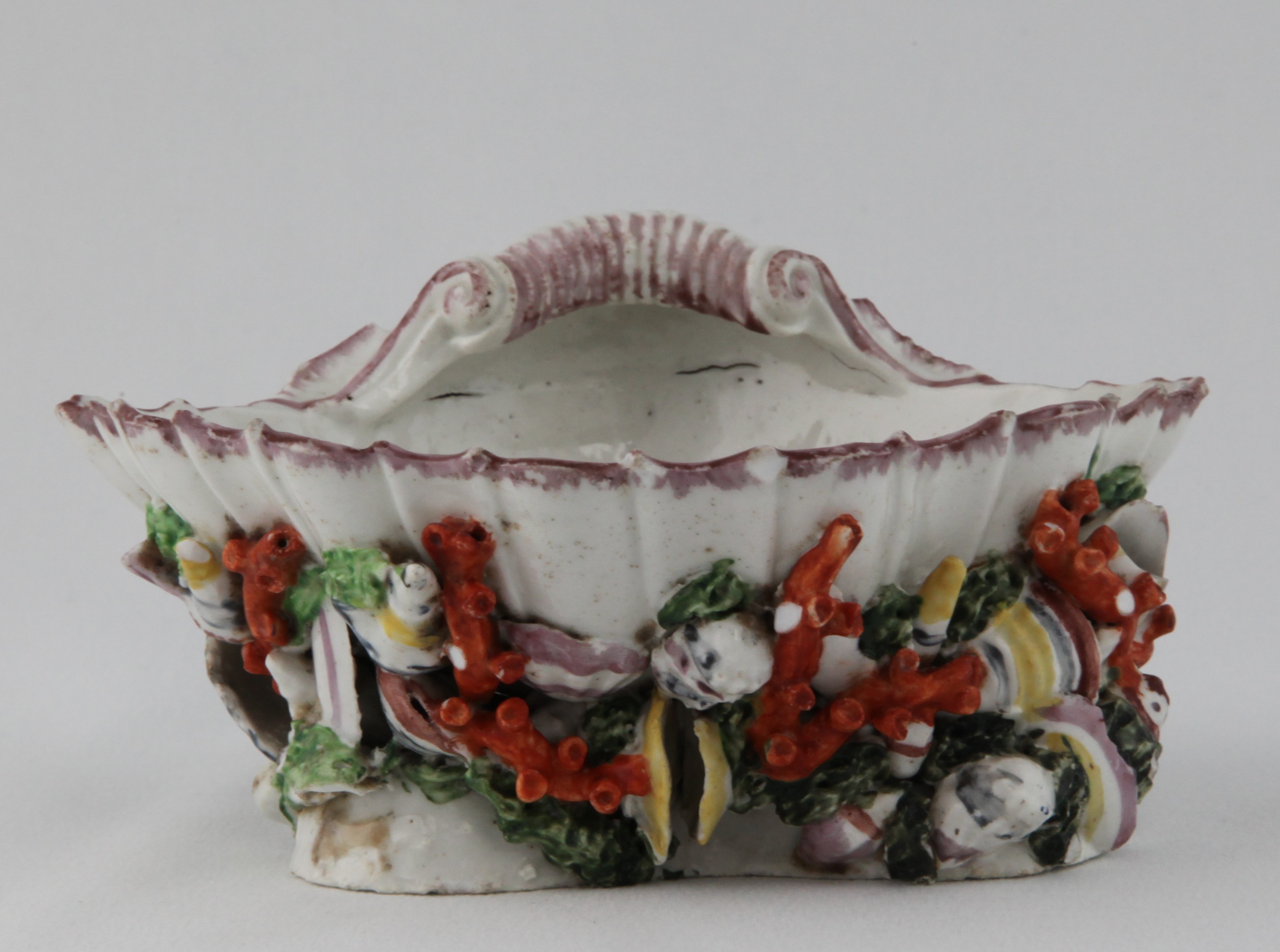 A rare Bristol scallop shell shaped sweetmeat dish, the interior painted in coloured enamels with a spray of flowers and leaves, the triform base finely modelled with brightly coloured naturalistic sea shells, coral and seaweed, the rim with a puce band, 6" wide, circa 1774-75, no mark. See Albert Amor, The Alfred Trapnell Collection, 1912, numbers 74, for a pair of Bristol dishes of this form