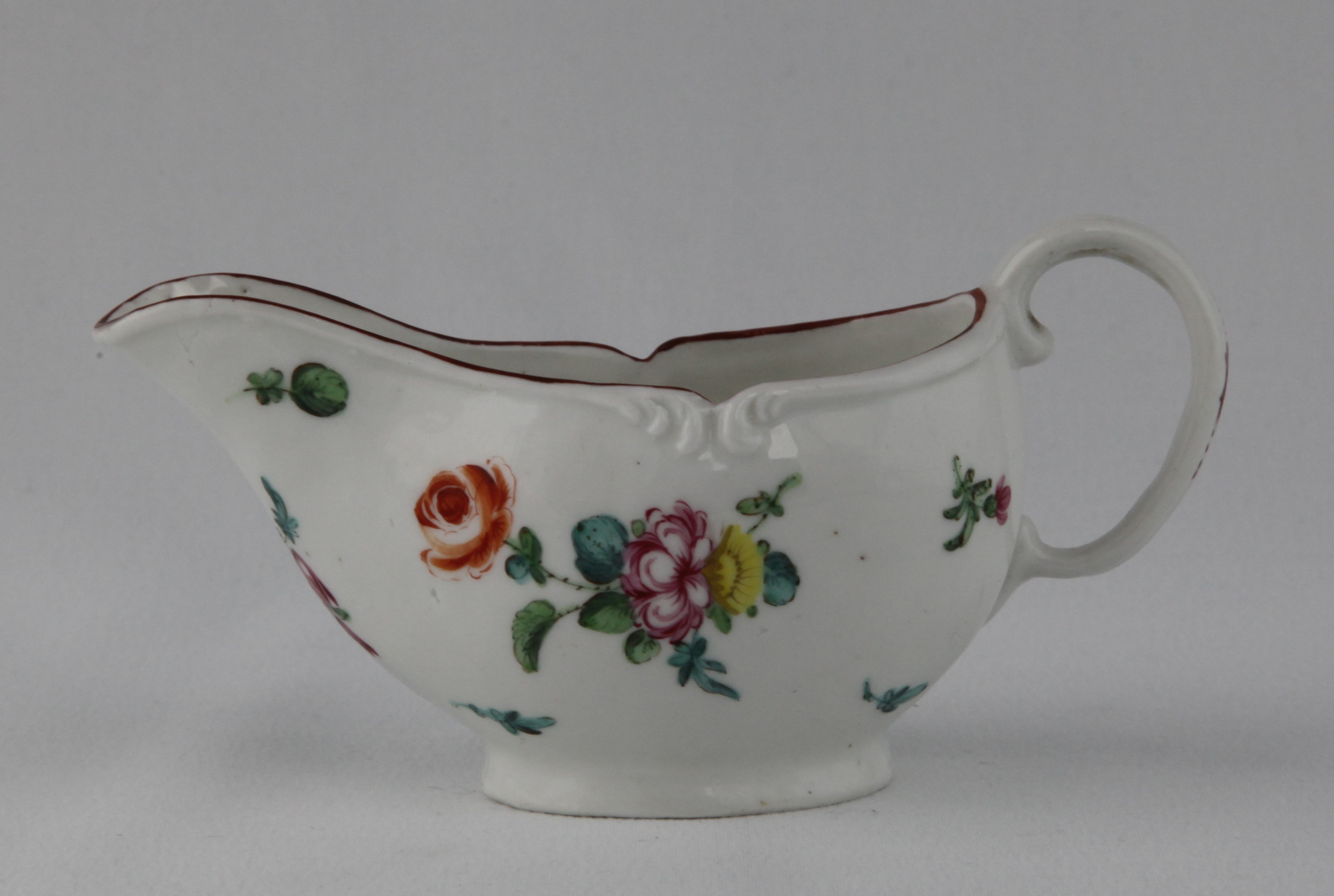 A Bristol small oval sauceboat, with 'C' scroll loop handle, painted in coloured enamels with two sprays of flowers and leaves, and scattered flowers, beneath a scroll moulded rim, painted with a brown band, 5" long, circa 1775, no mark