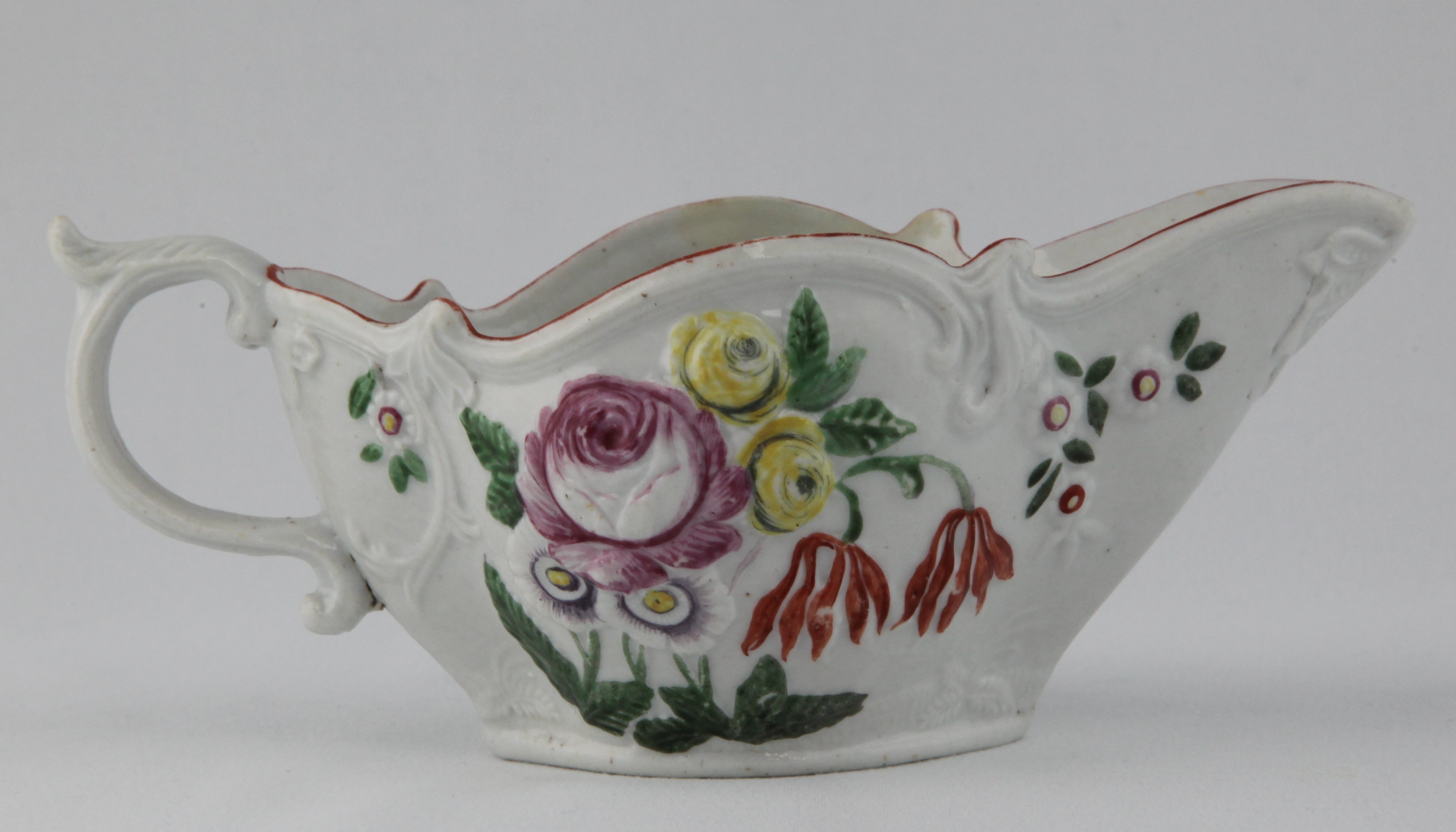 A Bristol oval sauce boat, the 'S' scroll handle with leaf moulded thumb piece, moulded in relief to both sides with a spray of flowers and leaves, boldly picked out in coloured enamels, within scroll moulded borders, beneath a brown line rim, 7 1/4" long, circa 1772, no mark