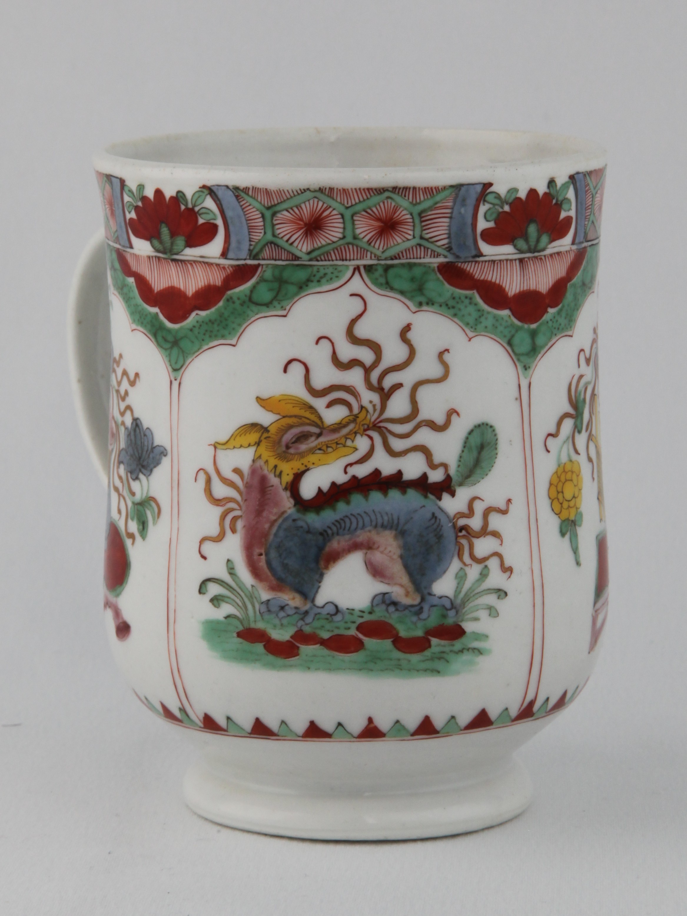 A Plymouth baluster shaped mug, with notched loop handle, painted in Chinese famille verte palette with the Dragon in Compartments pattern, 4 1/4" high, circa 1770, painted tin mark in red