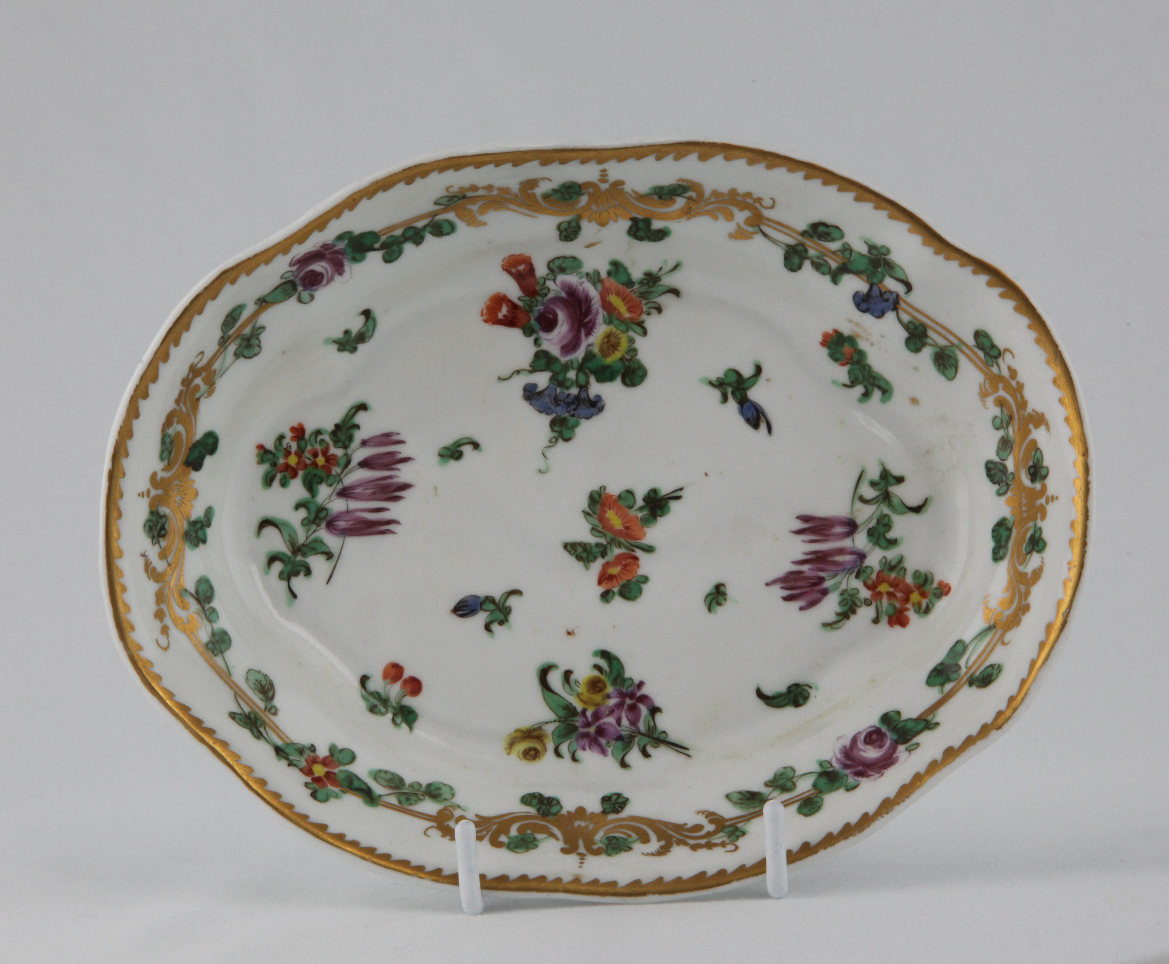 A rare Bristol oval spoon tray, painted in coloured enamels with scattered flowers and leaves, within a gilt band entwined with flowers and leaves, angular gilt dentil rim, 6 1/2" wide, circa 1772, no mark