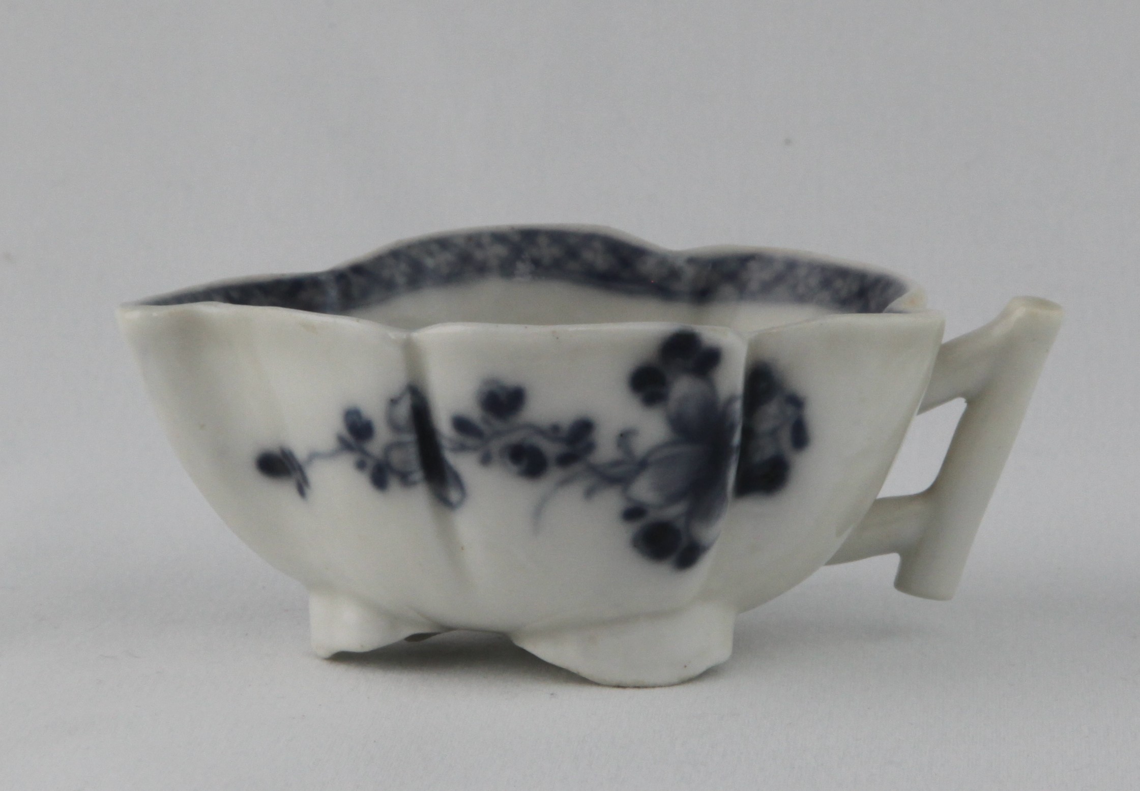 A rare Plymouth leaf shaped small asparagus butter boat, with angular stalk loop handle, painted in underglaze blue with two trailing flower sprays, the interior painted with a flower, within a diaper border, on three short feet modelled as scrolling leaves, 4 1/8" long, circa 1770. See Bernard Watney, English Blue and White Porcelain of the 18th Century, plate 94 (C), for a similar butter boat