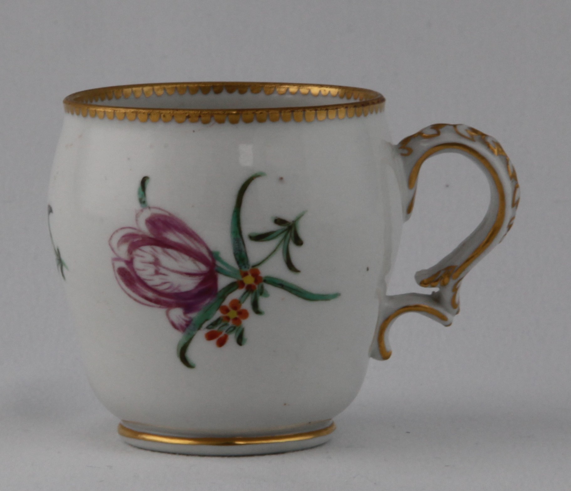 A Bristol ogee shaped coffee cup, with harebell moulded scroll handle, painted in coloured enamels with a flower spray and scattered flowers, within gilt line and dentil borders, 2 3/4" high, circa 1775, blue painted X and numeral 18
