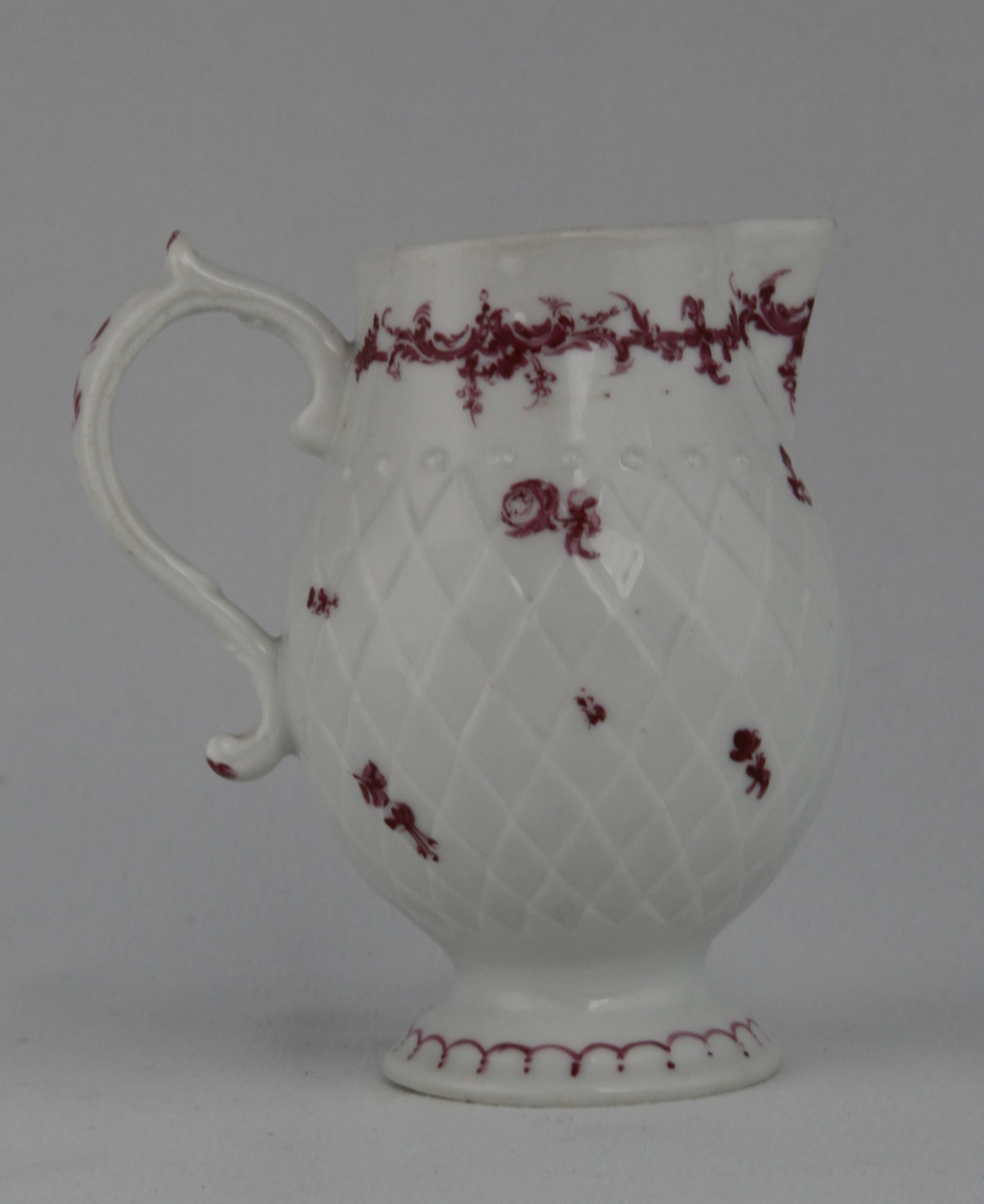 A rare Bristol baluster shaped sparrow beak milk jug, the 'S' scroll handle with scroll thumbpiece, painted in puce monochrome with scattered flowers, on a pinecone moulded ground, beneath a flower and 'C' scroll band, the spreading foot painted with a looped band, 3 3/4" high, circa 1772, no mark