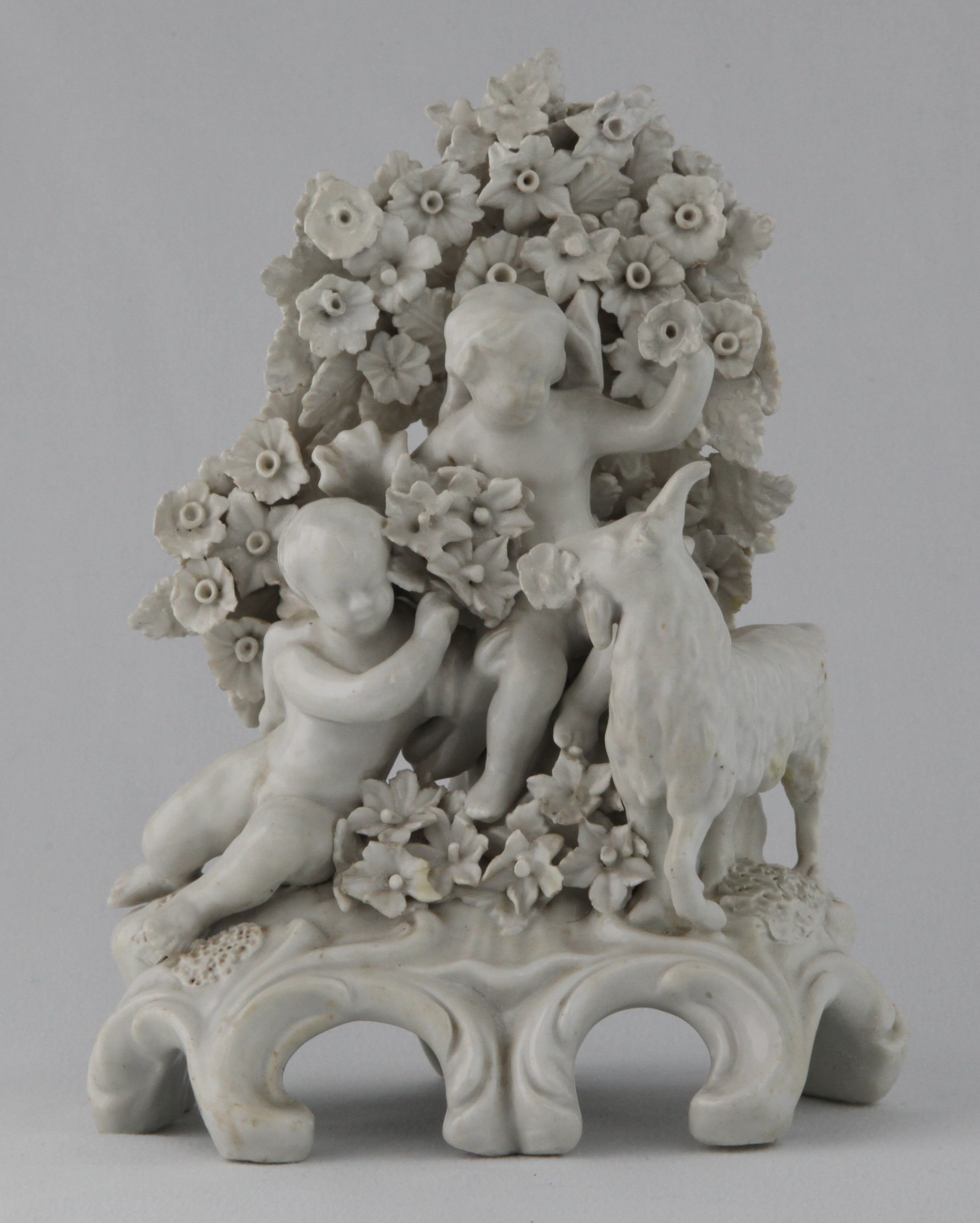 A Plymouth group of two putti and a goat, in the white, before floral bocage, on scroll moulded base, 7 1/2" high, circa 1770, no mark