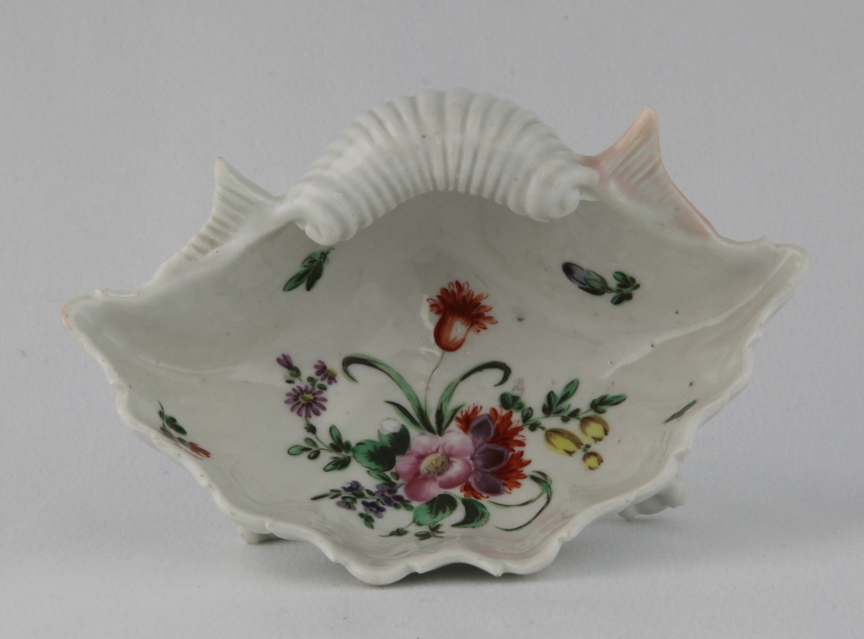A rare Bristol shell shaped salt, the interior painted in coloured enamels with a spray of flowers and leaves and scattered flowers, on three claw and ball feet. Circa 1775, blue painted X mark and numeral 6.