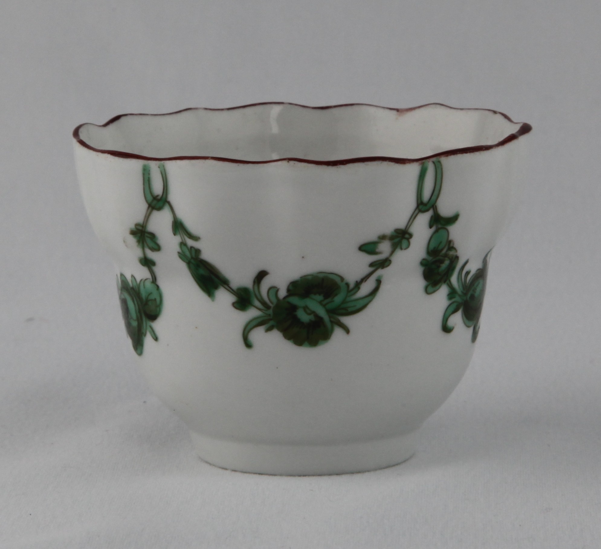 A Bristol small ogee shaped tea bowl, painted in green and black with floral garlands suspended from rings, within brown line rims, circa 1775, blue painted X marks and numeral 1