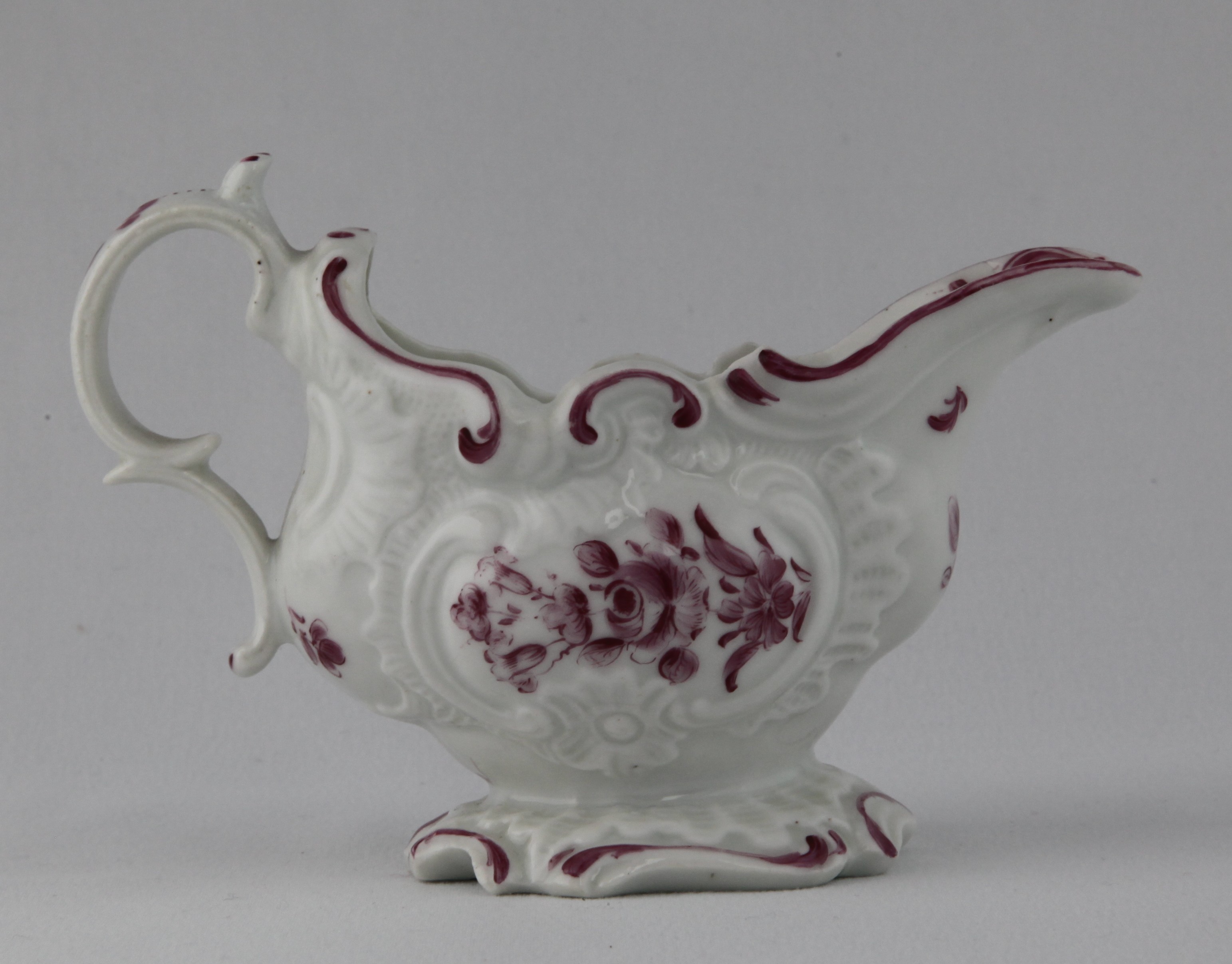 A Plymouth oval sauceboat, with 'C' scroll handle, with scroll thumb piece, painted in puce monochrome with flowers and leaves, within 'C' scroll moulded cartouches, beneath a scroll moulded rim, on spreading foot, the lip painted with a flower head and leaf scrolls, 5 1/2" long, circa 1770, no mark