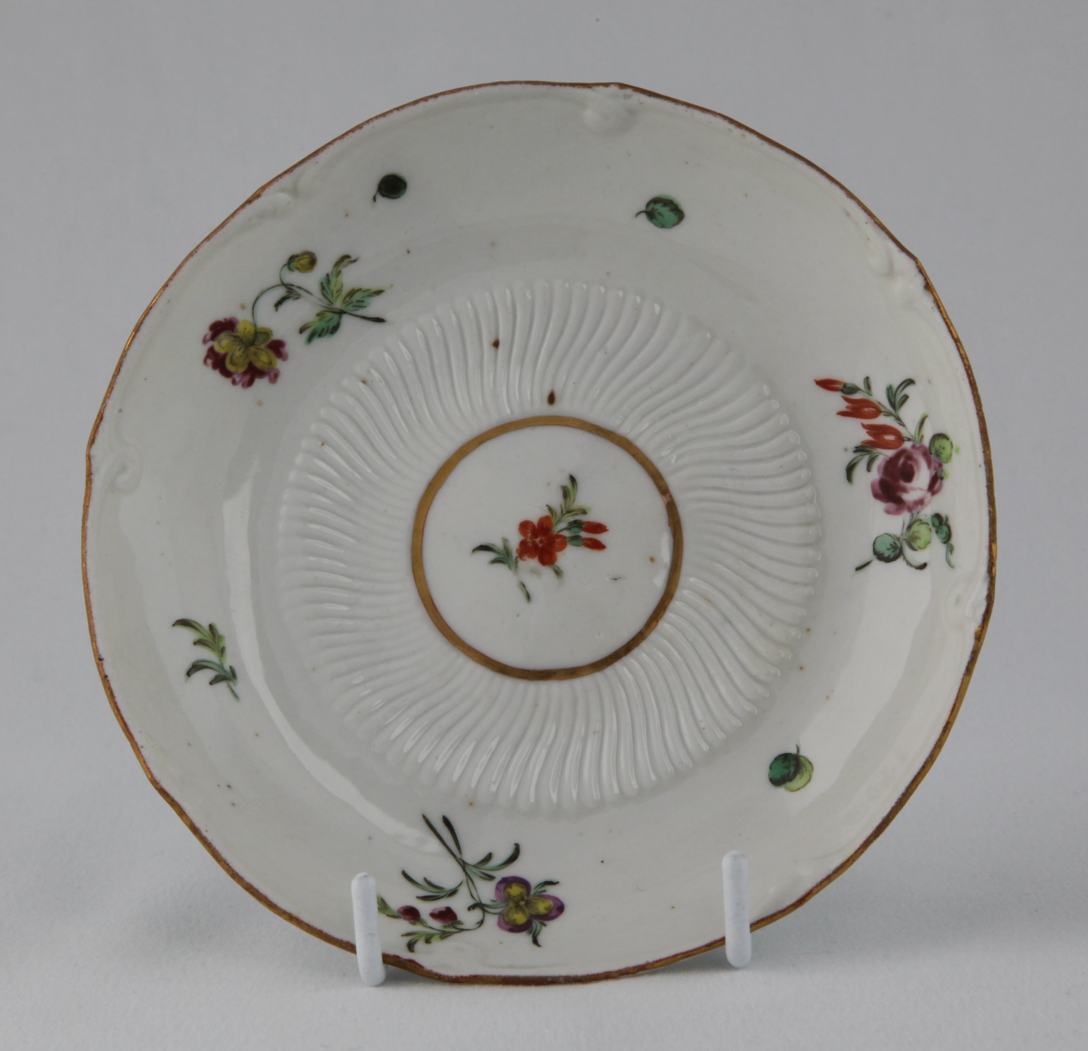 A rare Bristol saucer, very finely moulded with spirally fluted bands, and painted in coloured enamels with scattered flowers and leaves, within moulded borders with gilt line rims, circa 1772, blue painted X marks and numeral 7 in gilt