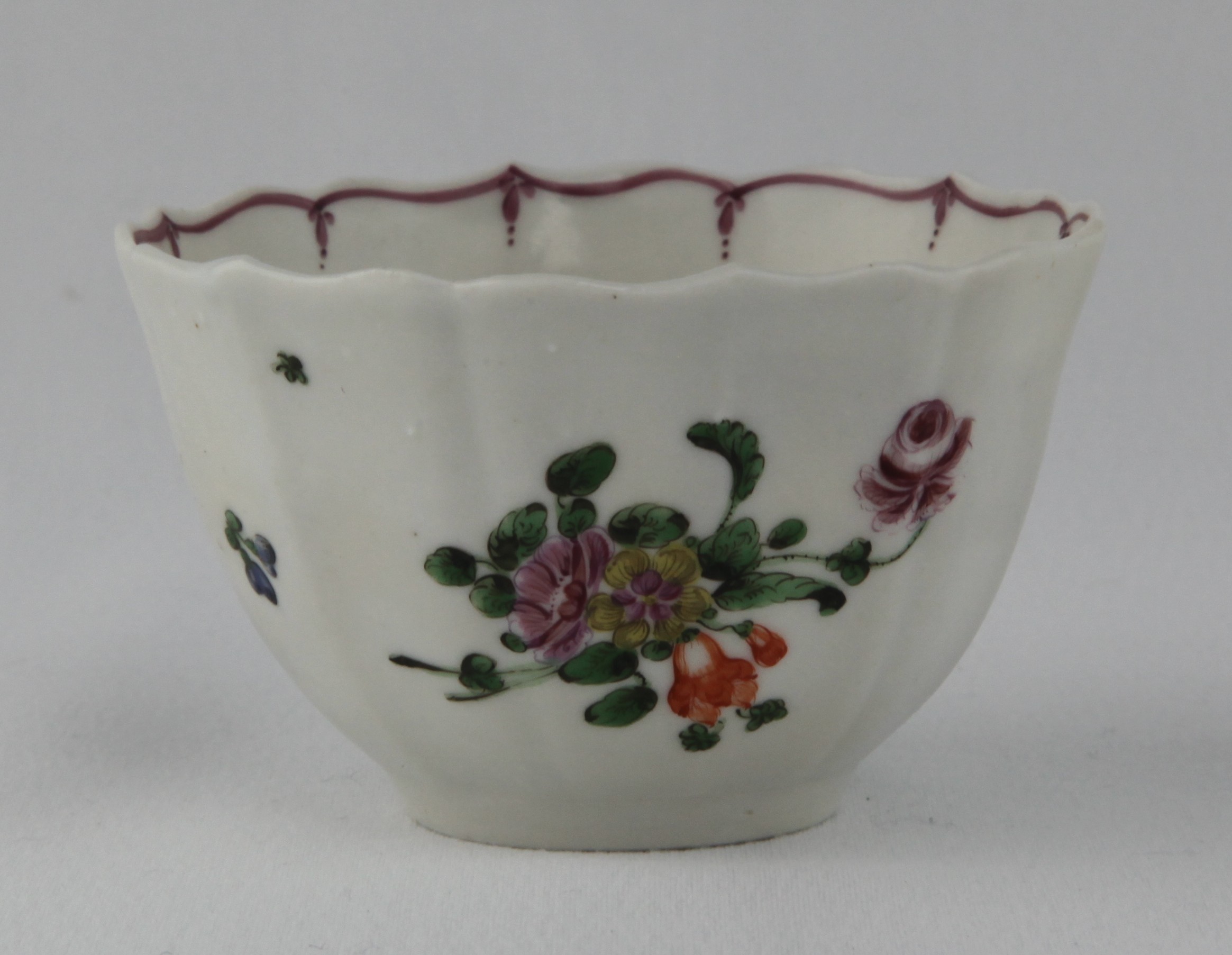 A rare Bristol tea bowl, of simple fluted form, painted in coloured enamels with sprays of flowers and leaves, and scattered flowers, within puce line and pendant borders, circa 1775, no marks