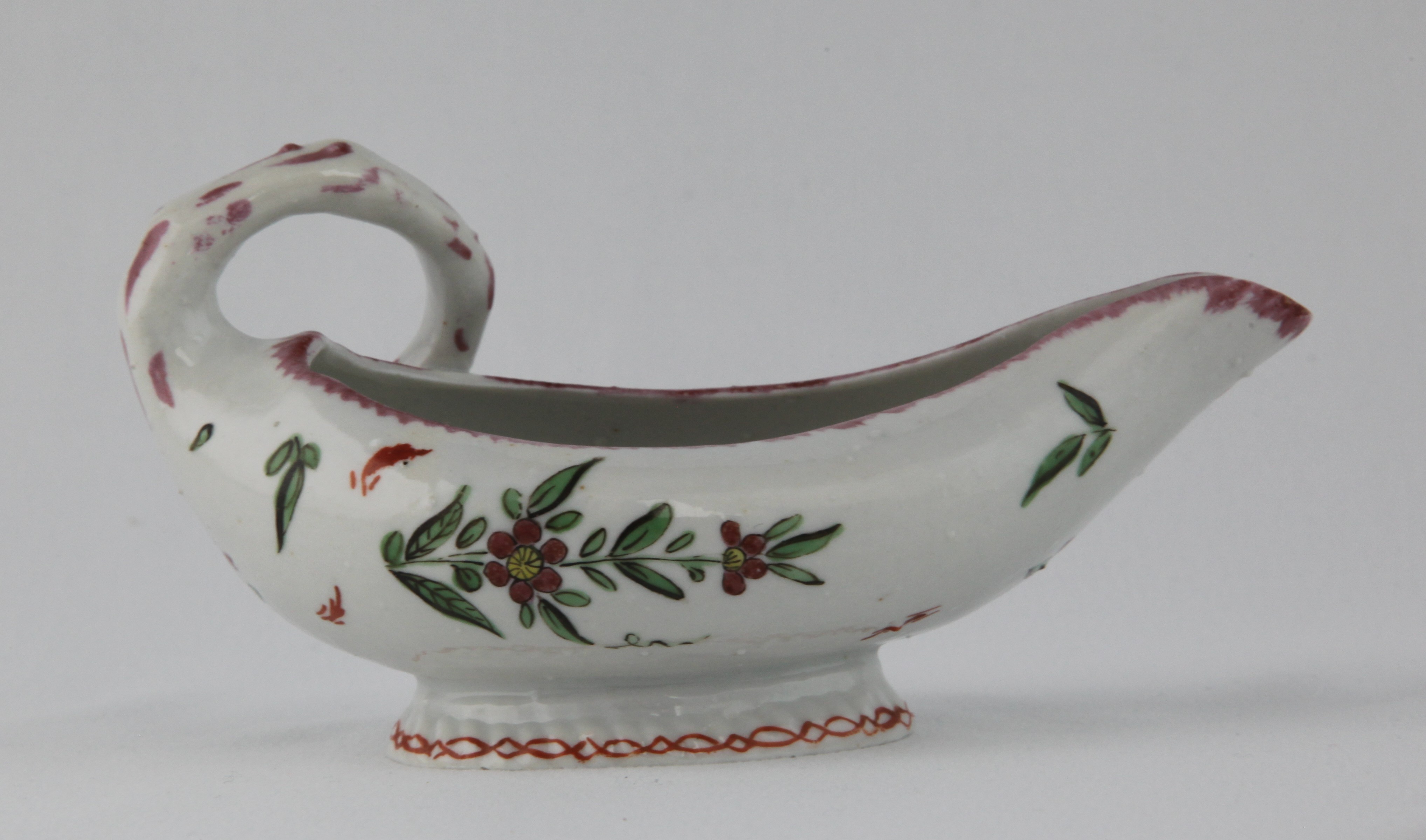 One of a pair of Bristol small leaf shaped sauceboats, each with stalk loop handle, painted in coloured enamels with flowers and leaves, beneath a puce feuille de choux border, each foot with an iron red interlinked band, 5 1/2" long, circa 1772, no marks