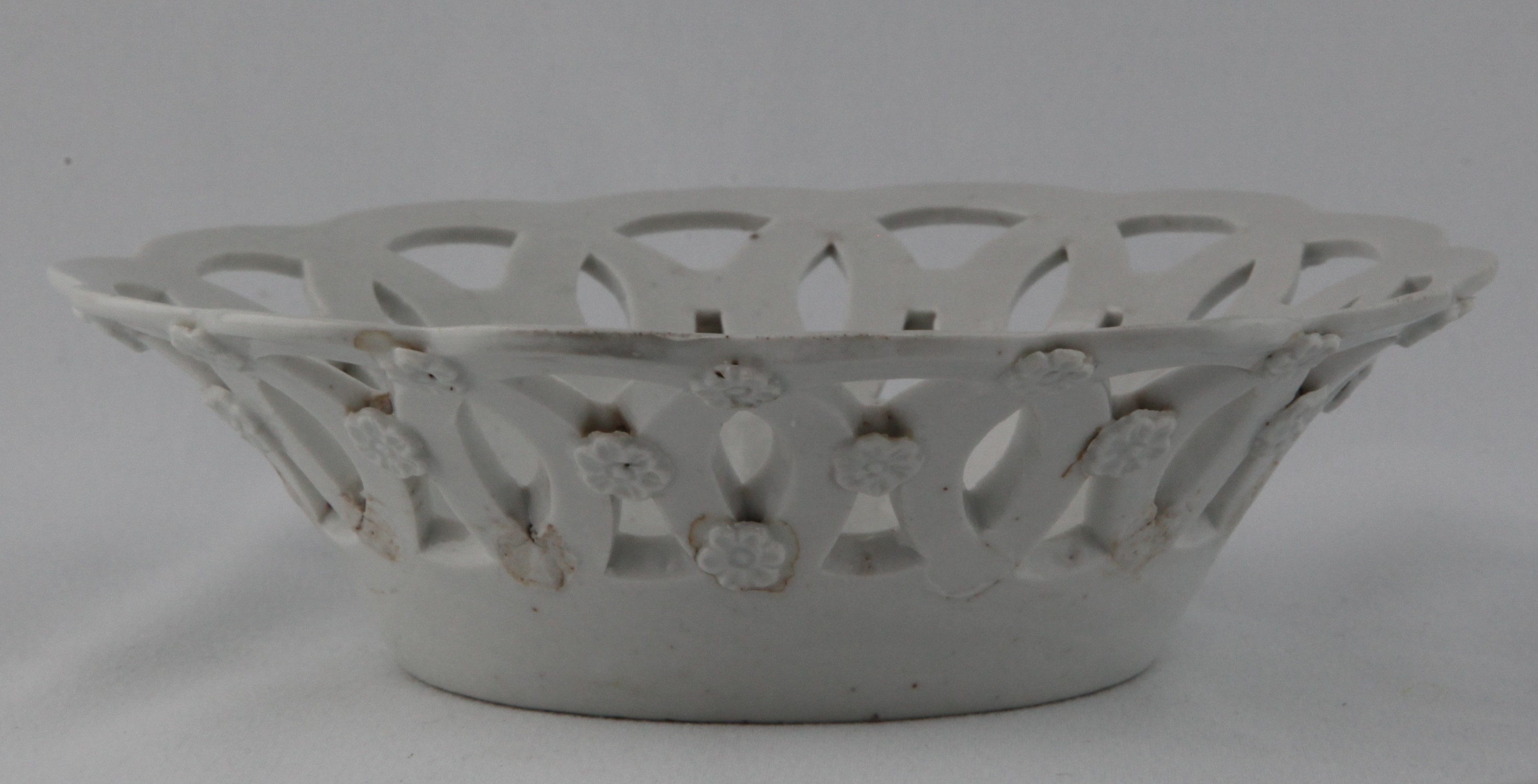One of a rare pair of Bristol shallow round baskets, after Worcester originals, in the white, each pierced with interlinked roundels, the exterior applied with flower heads, 6 3/4" diameter, circa 1772, no mark