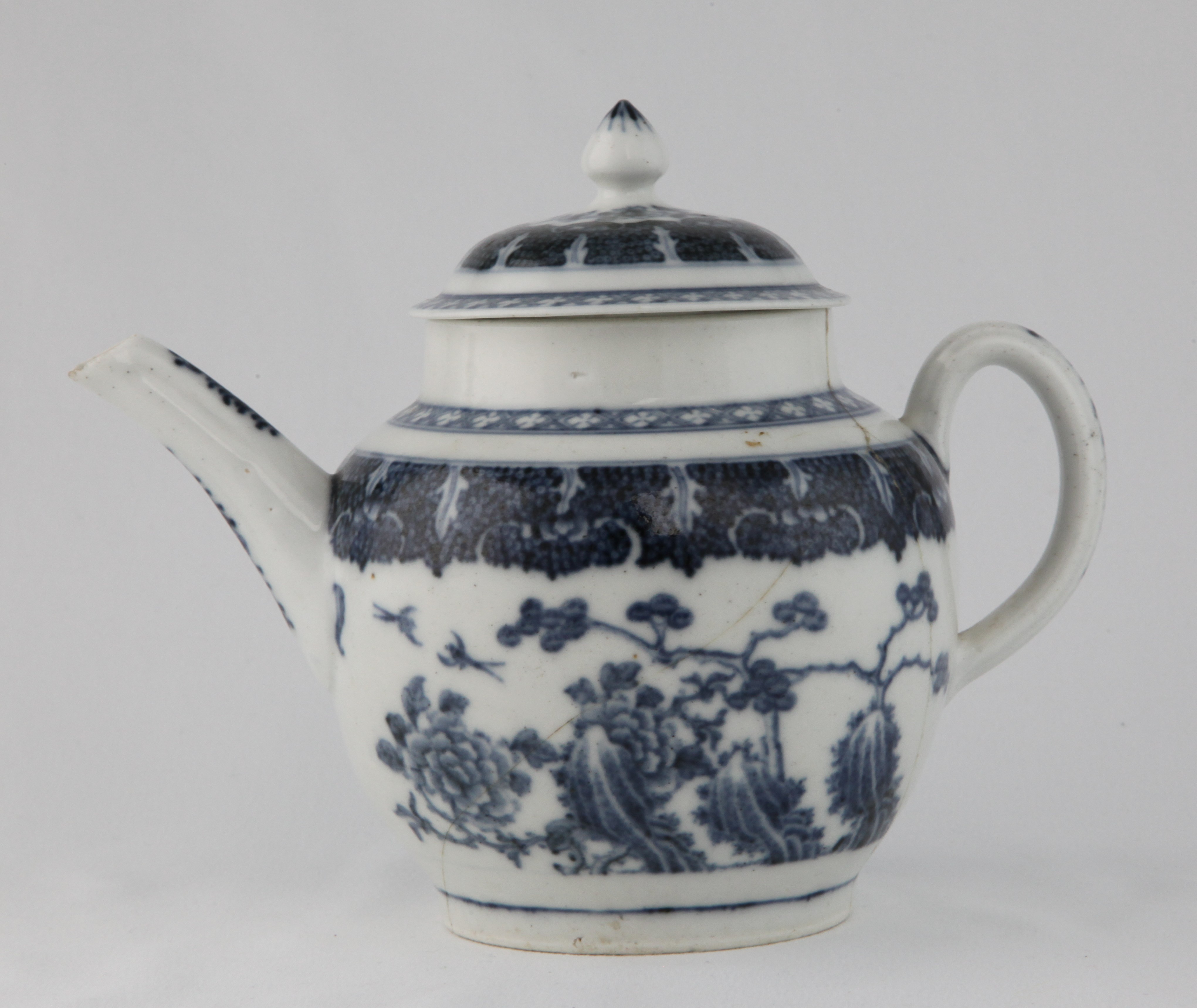 A Plymouth globular teapot and domed cover, with loop handle and pointed knop, finely painted in underglaze blue in Chinese style with pine, peony and rockwork, within broad cell diaper bands, with flowers and leaves, and diaper borders, 6 1/2" high, circa 1770, inscribed beneath with repairers mark for 'Coombes, Queen Street, Bristol' and dated 1801