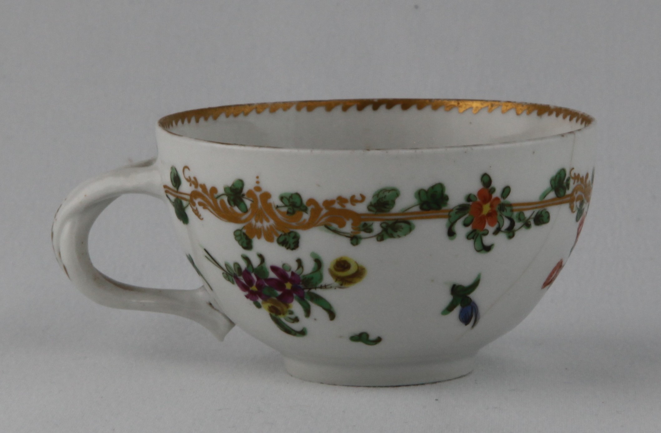 A Bristol ogee shaped teacup,  with entwined handle, painted in coloured enamels with sprays of flowers and leaves, and scattered flowers, within a gilt band entwined with flowers and leaves, angular gilt dentil rim, circa 1772, no marks