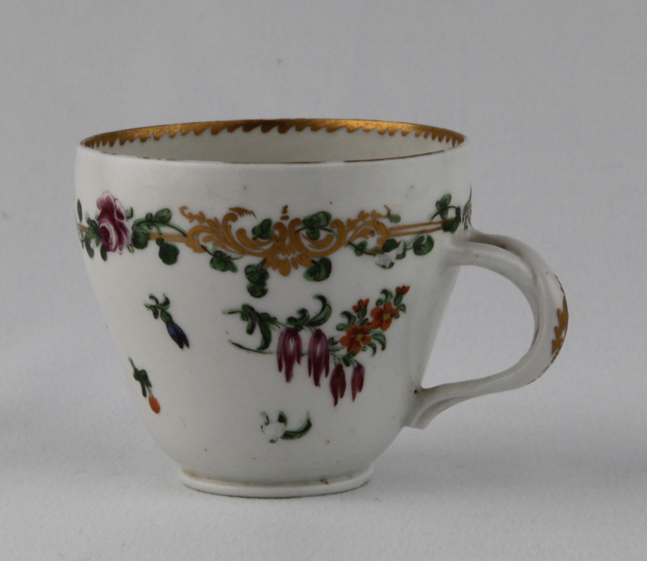 A Bristol ogee shaped coffee cup, with entwined handle, painted in coloured enamels with sprays of flowers and leaves, and scattered flowers, within a gilt band entwined with flowers and leaves, angular gilt dentil rim, circa 1772, no marks