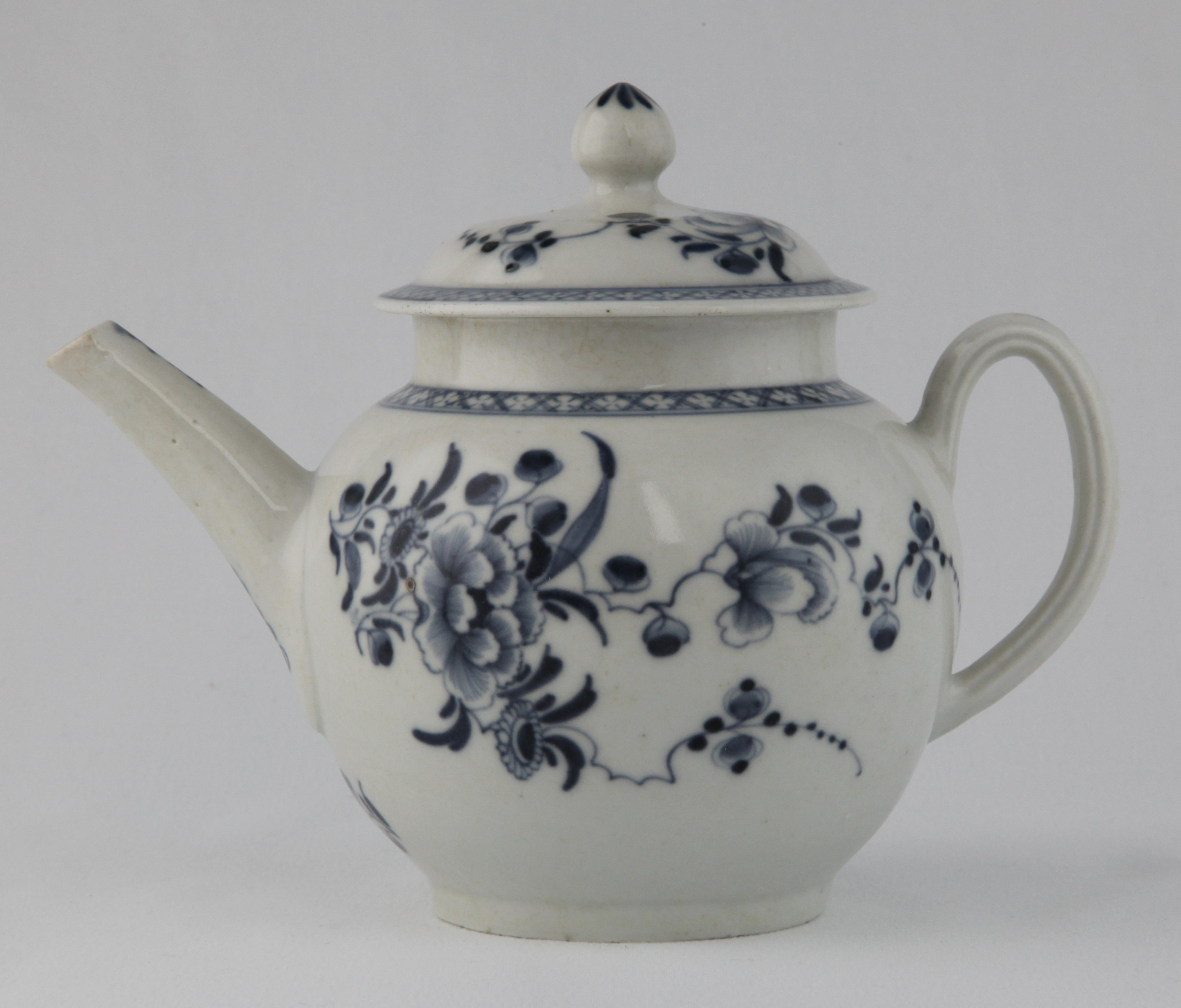 A Plymouth globular teapot and cover, with loop handle and pointed knop, painted in underglaze blue in Chinese style with trailing flowers and leaves, within diaper borders, 5 1/2" high, circa 1770, blue painted tin mark