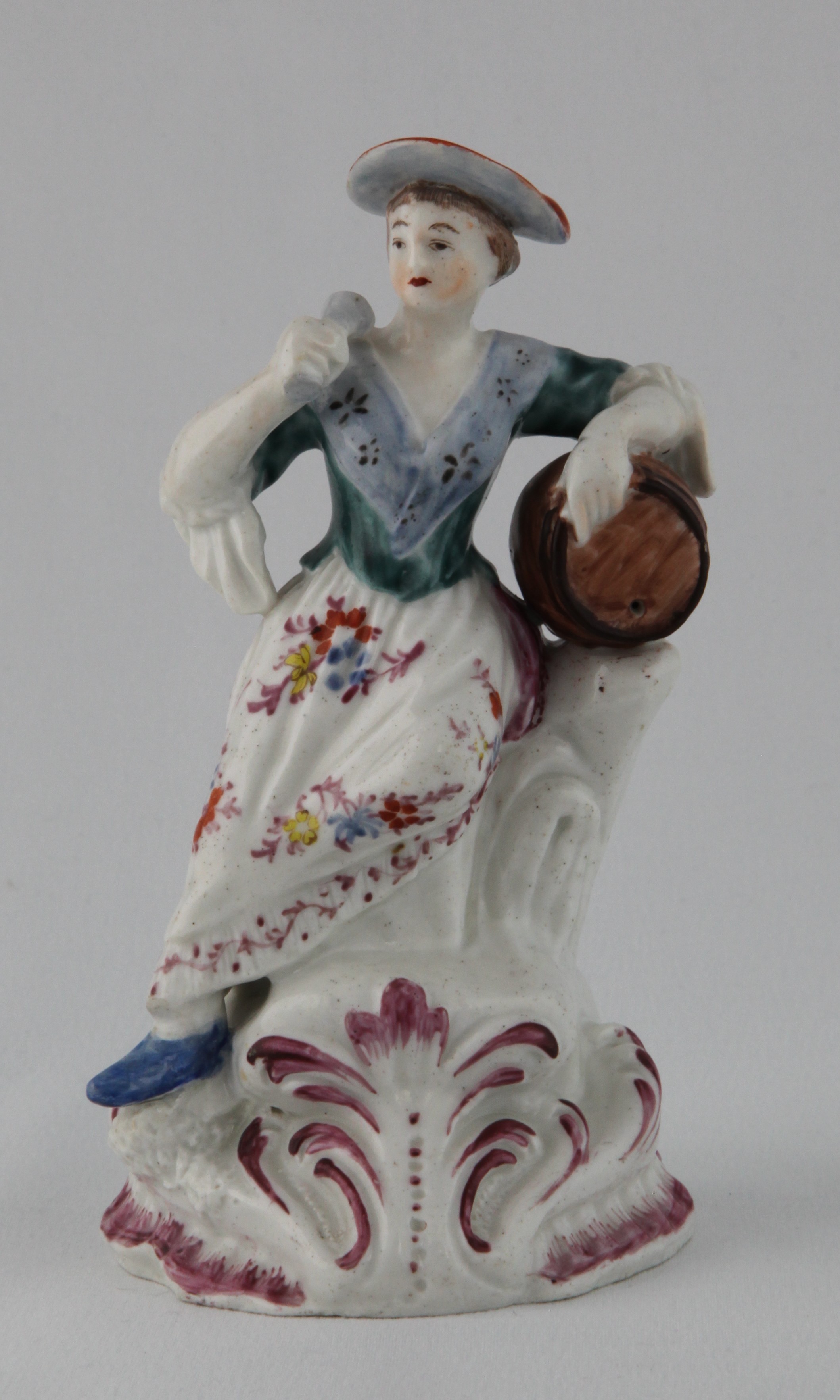 A Plymouth figure of a a female toper, a barrel under her left arm, and a glass in her right hand, decorated in coloured enamels, the high scroll moulded mound base picked out in puce, 5 3/4" high overall, circa 1770, no mark