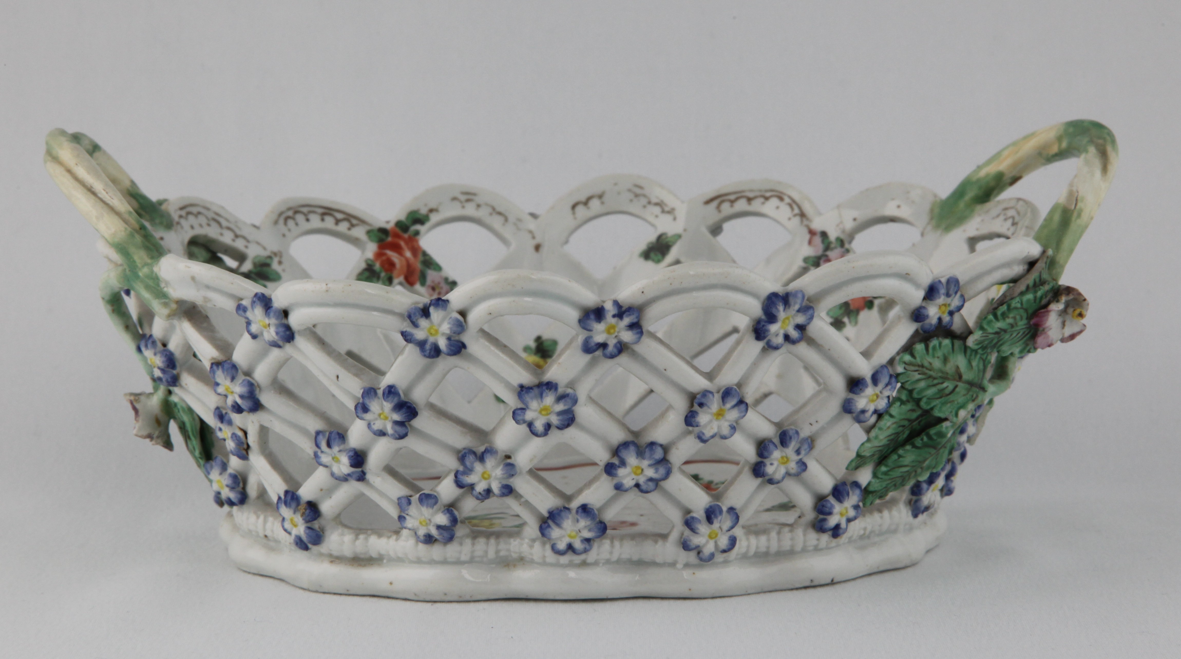 A Bristol pierced oval basket, in Worcester style, the two green glazed spiral twist loop handles with applied flower and leaf terminals, painted in coloured enamels with a spray of flowers and leaves, and scattered flowers, within a purple loop and dot border, the exterior applied with forget-me-not flower heads, picked out in blue and yellow, 8 1/2" wide overall, circa 1775, no mark