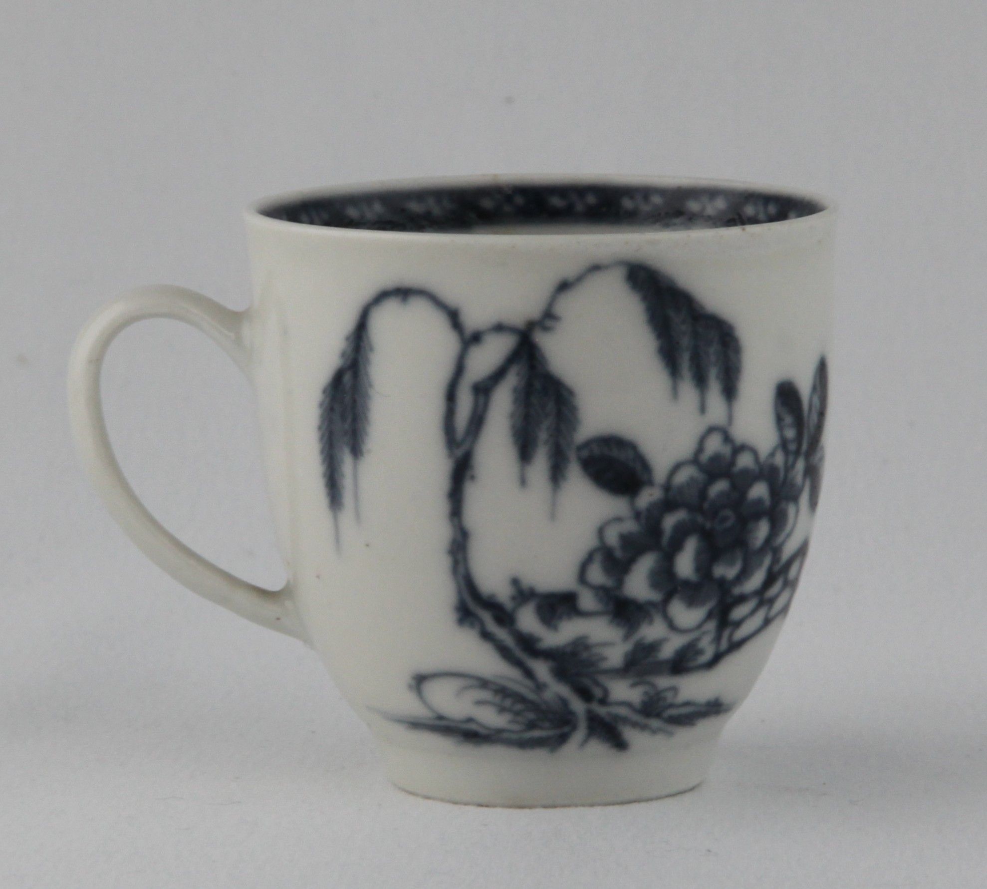 A Plymouth coffee cup, with loop handle, painted in underglaze blue in Chinese style with a fenced garden, with a pine tree and peony, the interior with a diaper border, 2 ¼” high, circa 1770. Named here as The Angled Fence Pattern