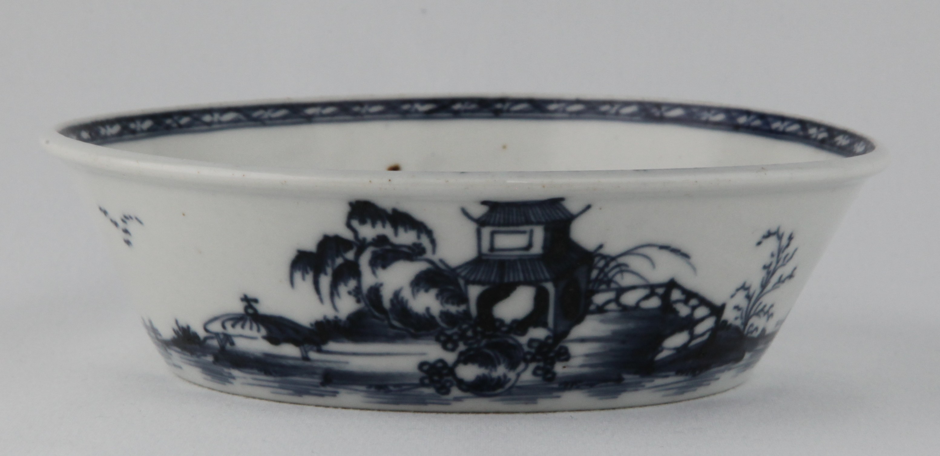 A Plymouth flared round tart pan, the exterior painted in underglaze blue in Chinese style with a pavilion, a willow tree and rockwork, with a fence, on an island, and with birds in flight and clumps of water reeds, 5 3/4" diameter, circa 1770