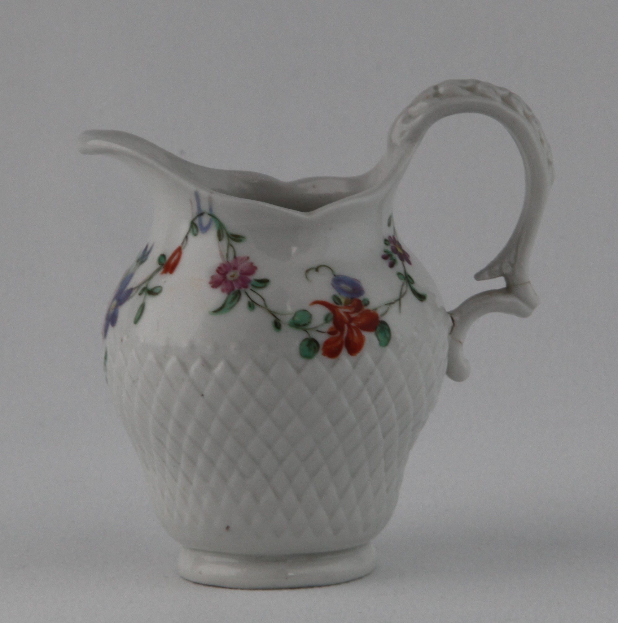 A Bristol small ogee shaped cream jug, with harebell moulded scroll handle, painted in coloured enamels with swags of flowers and leaves, above a broad pinecone moulded band, 3 1/4" high, circa 1775, blue painted X mark and numeral 14