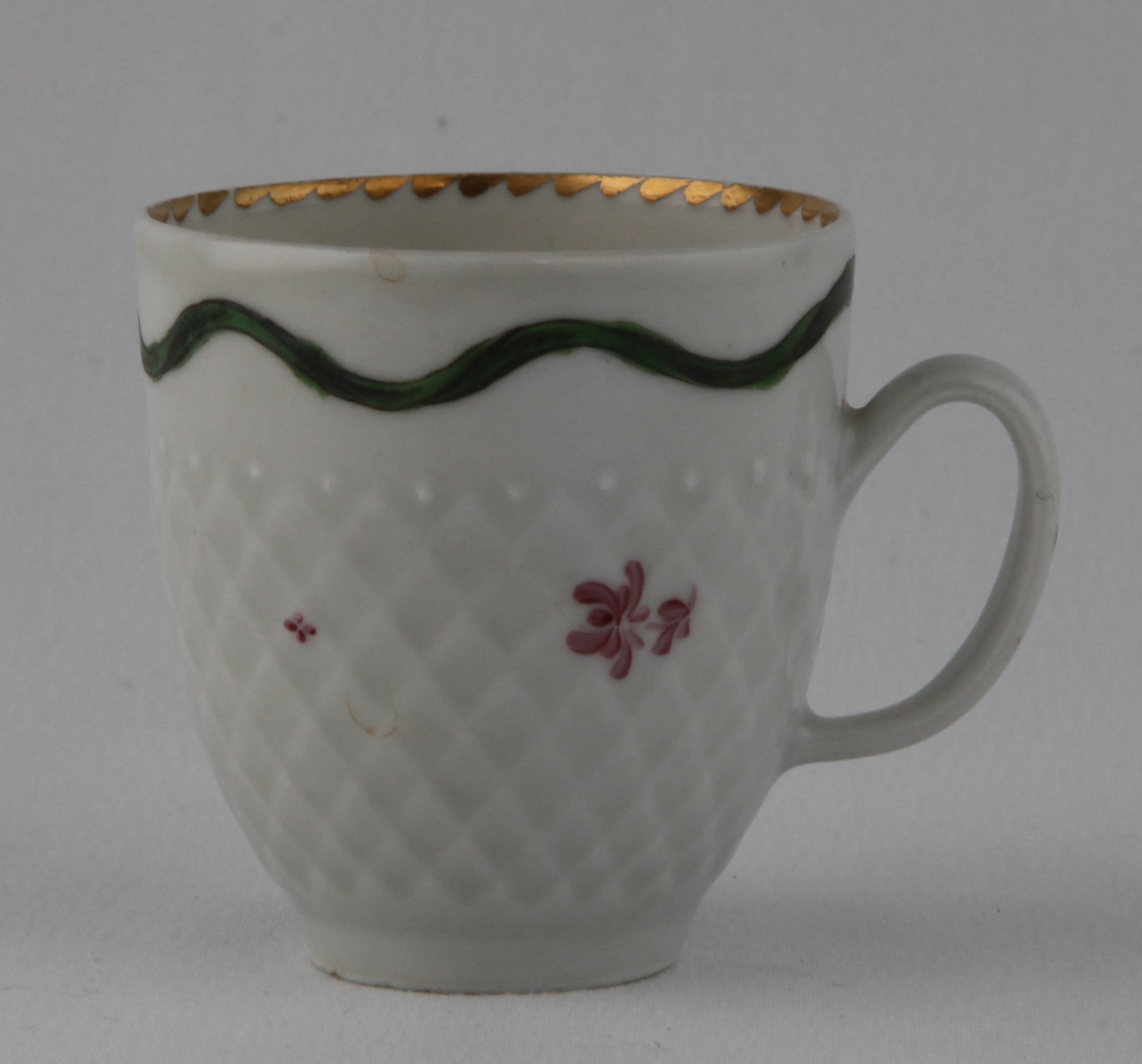 A Bristol pinecone moulded coffee cup, with loop handle, painted in puce monochrome with flower sprigs, beneath a wavy green band, the interior with an angular gilt dentil band, 2 3/8" high, circa 1775, no mark
