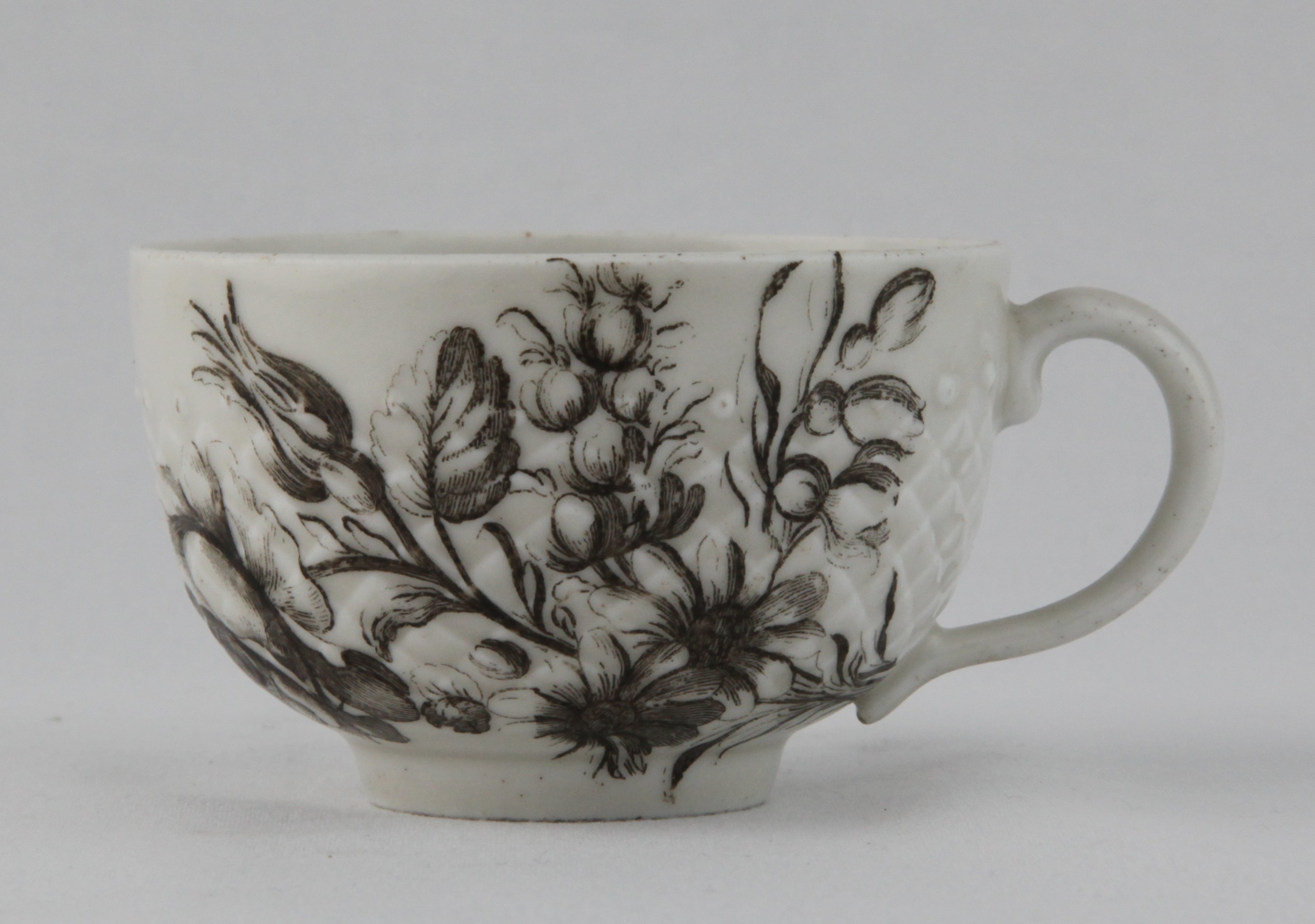 A rare Bristol tea cup, with ear shaped handle,  pinecone moulded and finely printed in black with a flower spray, and the cup printed with a butterfly, circa 1775, no mark