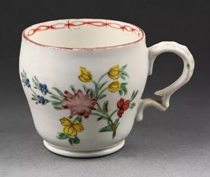 A Bristol coffee cup, of ogee shape and with harebell-moulded scroll handle, painted in enamels with a loose bouquet of flowers and scattered leaves, red rim line and red chain band to interior