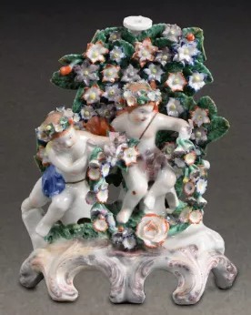 A Plymouth figural candlestick featuring two putti seated in front of bocage with a goat