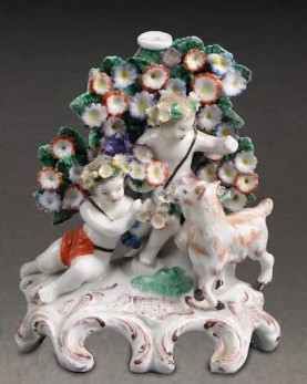 A Plymouth figural candlestick featuring two putti seated in front of bocage