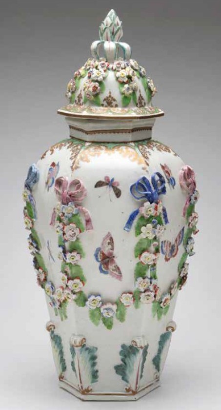A rare Plymouth large hexagonal baluster shaped vase and domed cover, with pinecone and leaf knop, painted in coloured enamels with butterflies and other winged insects, and a ladybird, with applied garlands of coloured flowers and leaves, suspended from puce and blue ribbon ties, within bright green and gilt flower and ‘C’ scroll borders, the base with stiff leaves, picked out in green, puce and gilt, 16” high, circa 1769-70, painted tin mark in iron red