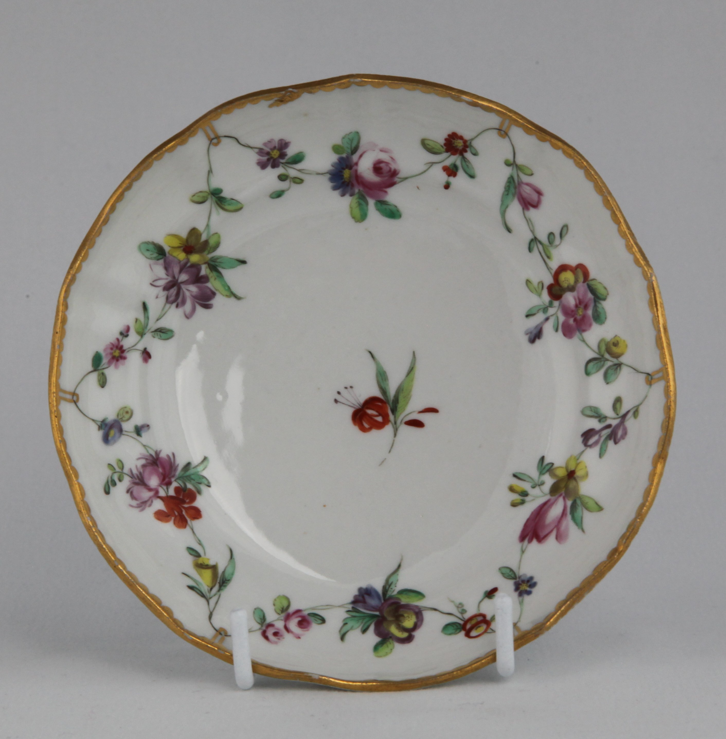 A Bristol saucer of lobed, ogee shape, painted in enamels with garlands of flowers suspended from gilt loops hanging from gilt dental rim