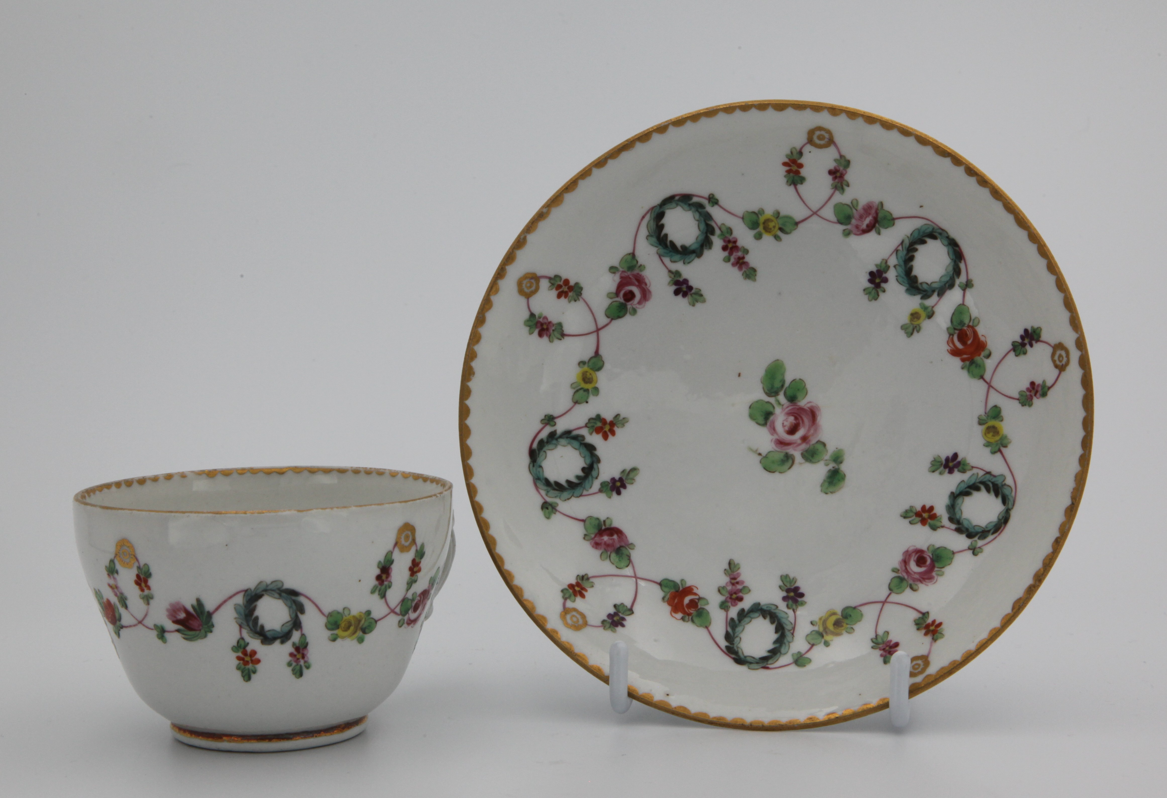 A very fine Bristol teacup and saucer with floral swags on a pink line, suspended from gilt roundels and looping over blue wreaths.