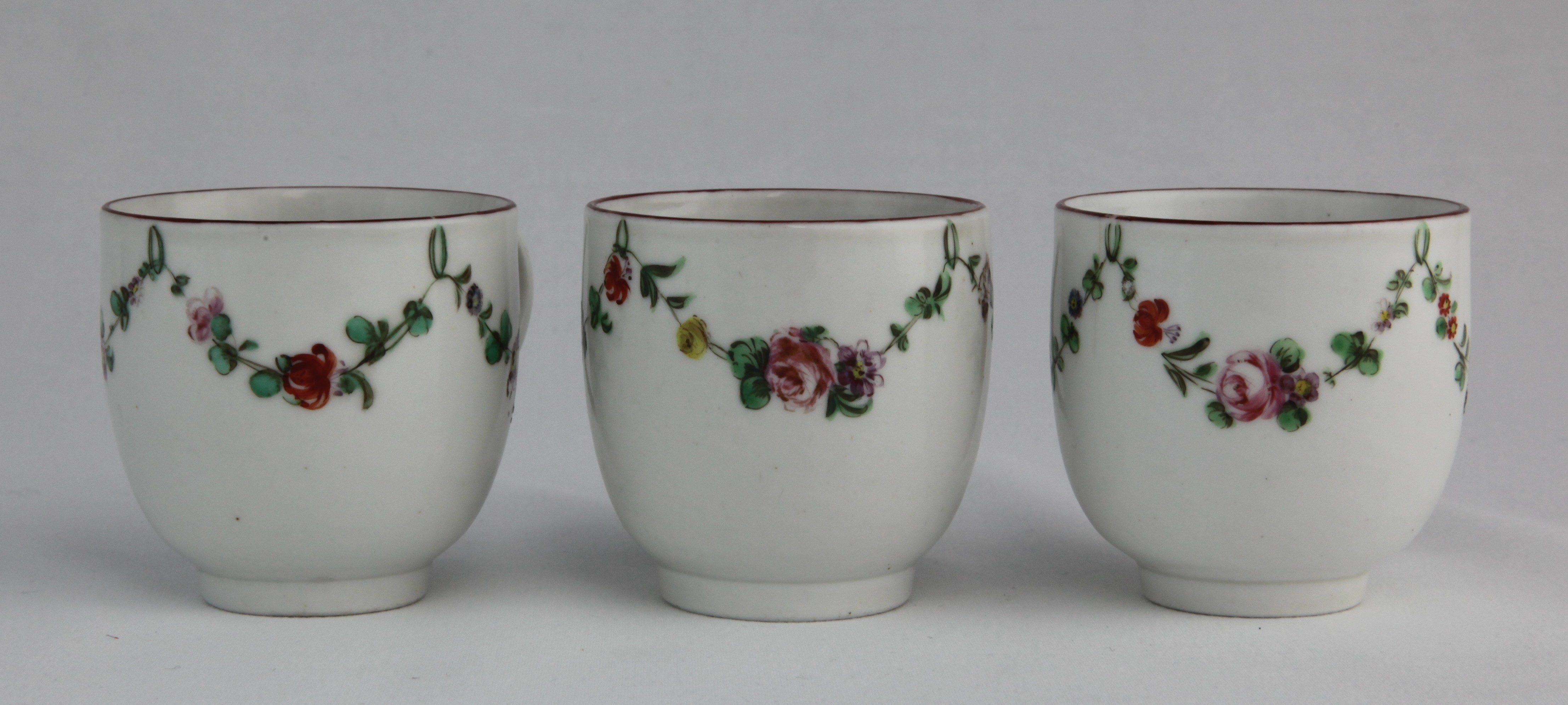 Three Bristol coffee cups with garlands of flowers suspended from green loops hanging from an iron red rim, all decorated by 16.