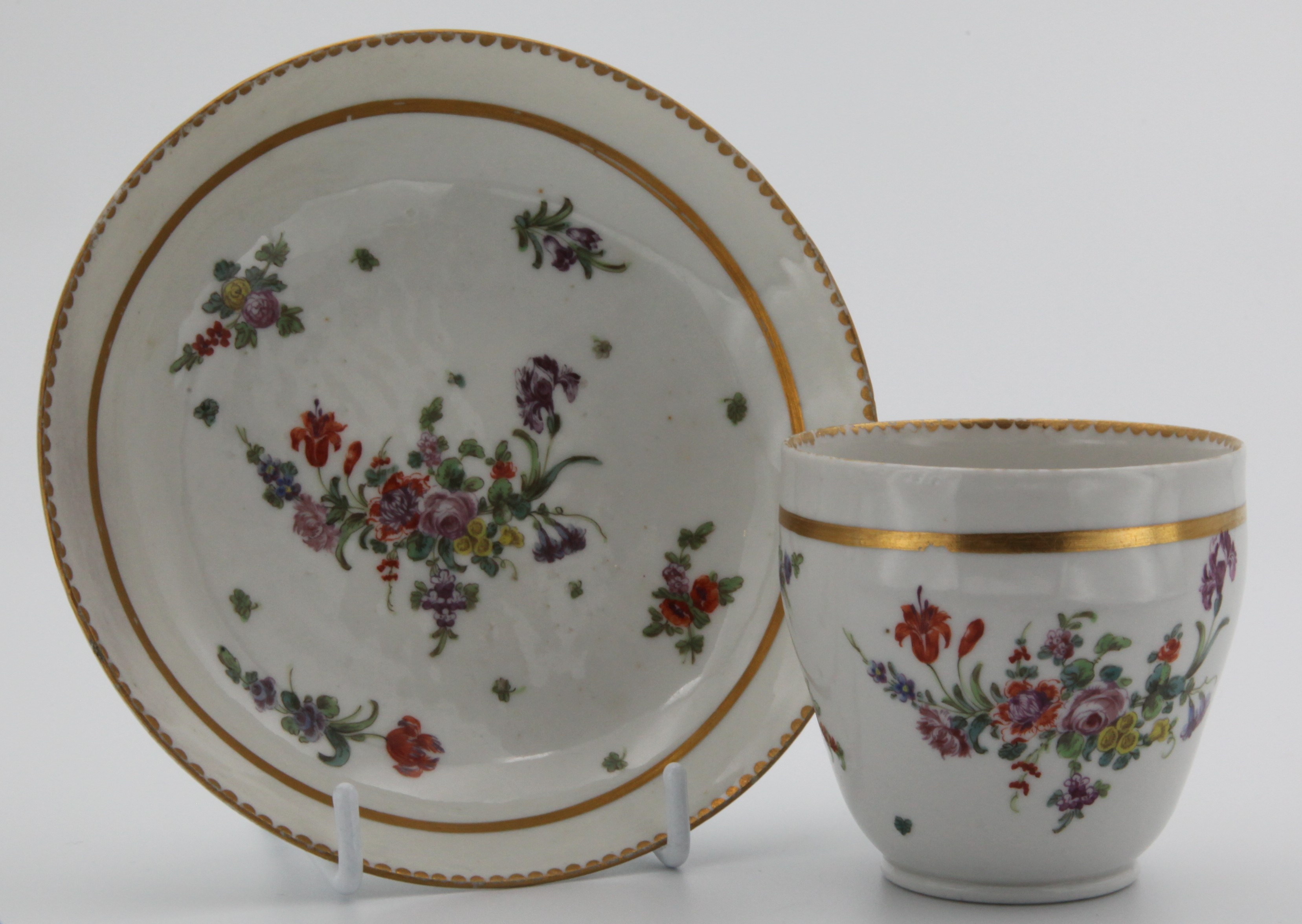 An ogee-shaped Bristol coffee cup and saucer with thick gilt band, floral sprays and gilt dentil rim