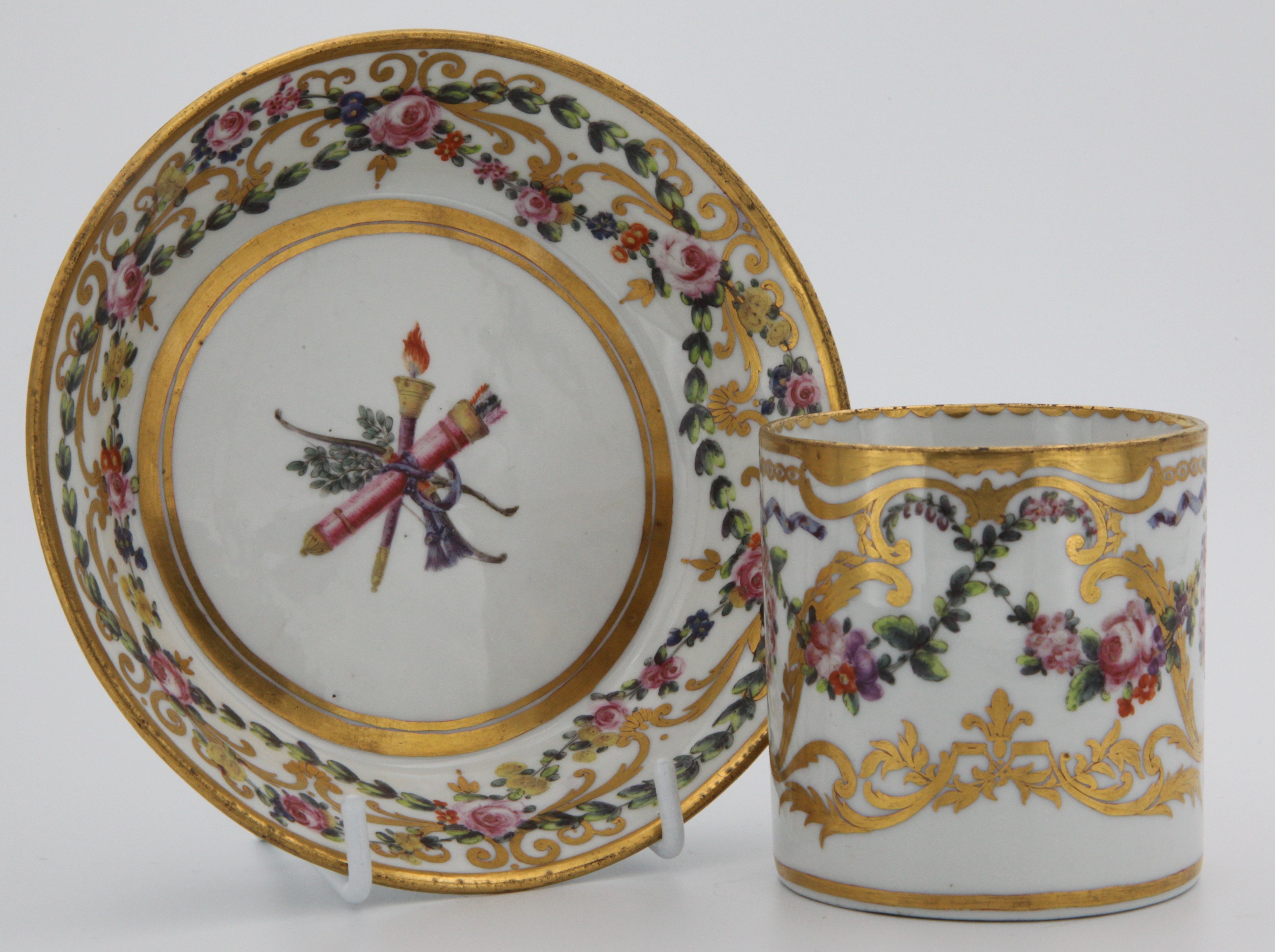 An extremely fine Bristol cabinet cup and saucer with swags of flowers and roundels of pink roses suspended from blue ribbons, within gilt leaf scrolls and a central trophy emblematic of Love.