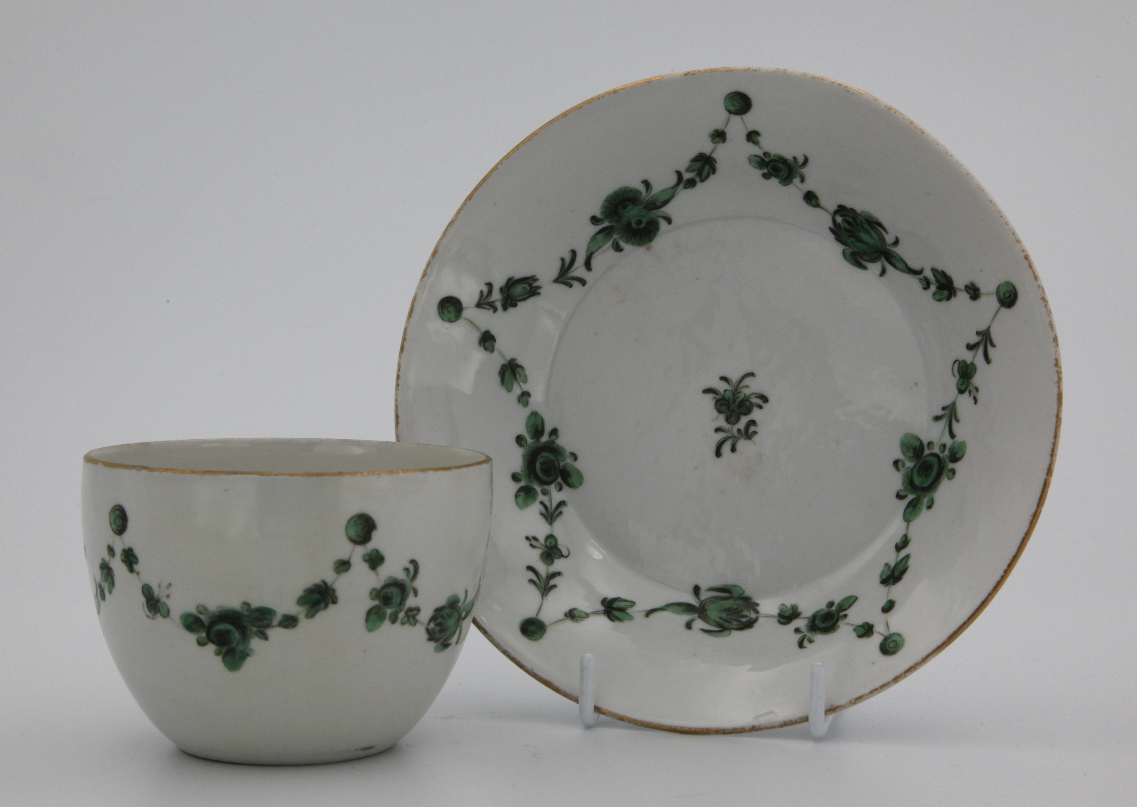 A Bristol tea cup and saucer with green garlands suspended from green roundels under a gilt rim line.