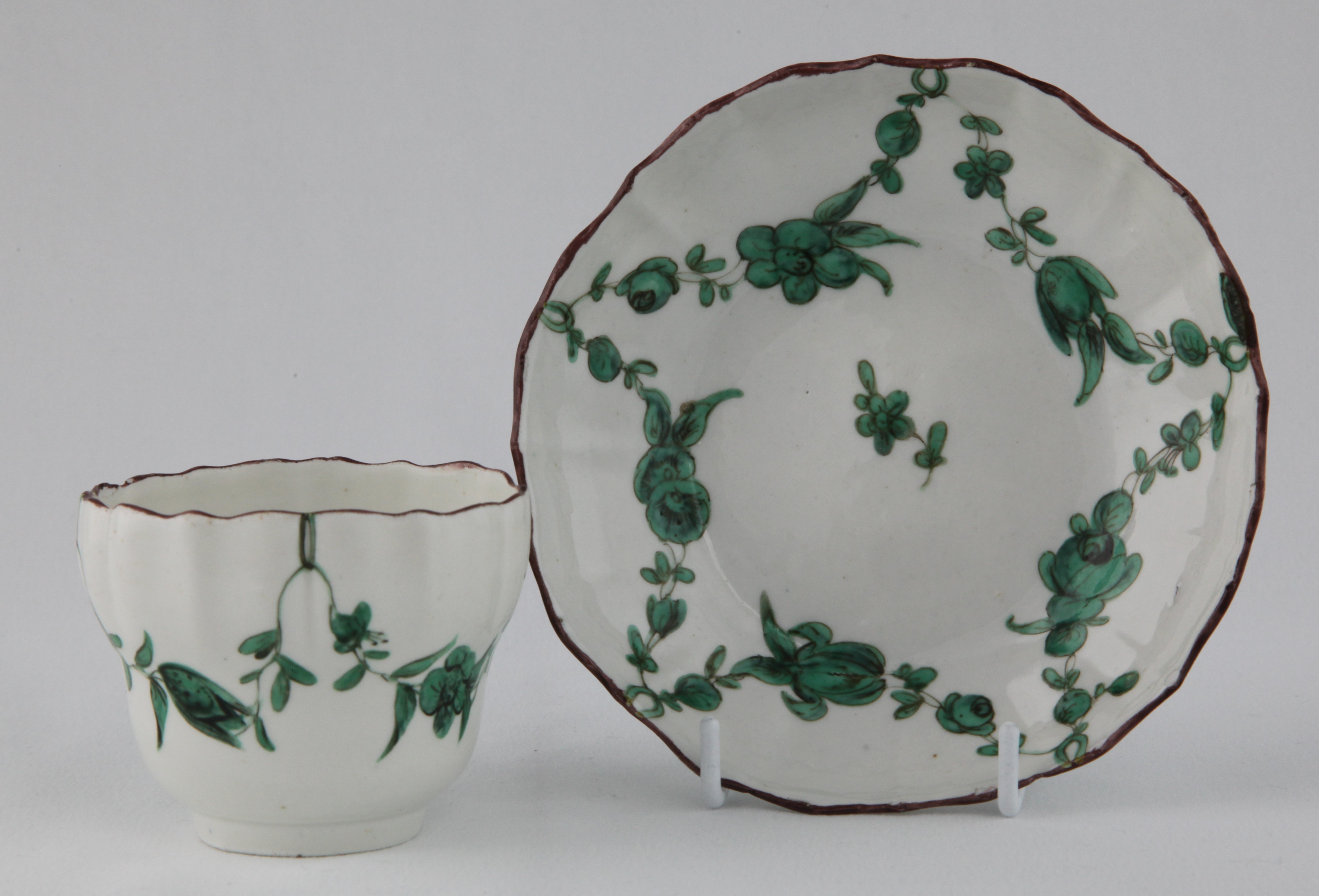A cup and saucer with green monochrome garlands suspended from green loops hanging from an iron red rim line